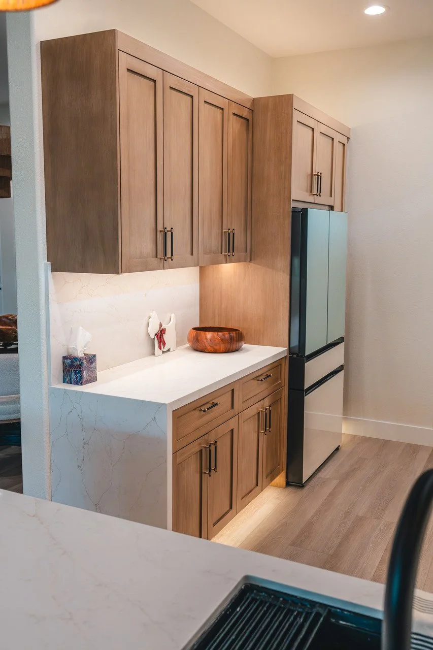 Kitchen corner with wooden cabinets, a white marble countertop, decorative items, and a stainless steel refrigerator.