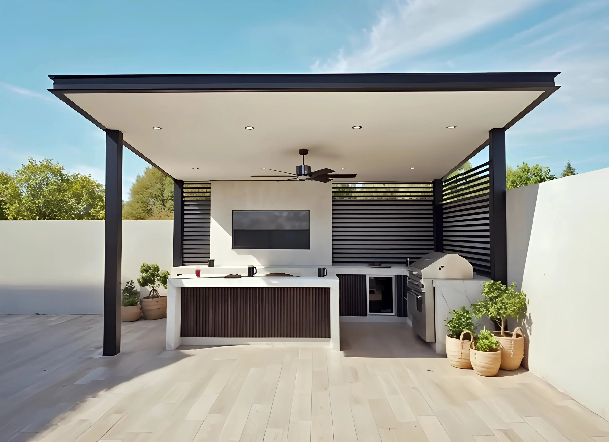 Modern outdoor kitchen with a built-in grill, counter space, and a wall-mounted TV, under a covered patio with ceiling fan and potted plants.