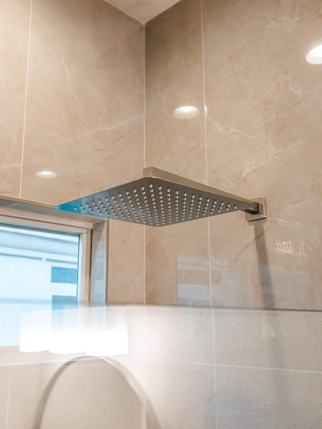 Close-up of a modern showerhead mounted on a beige tiled wall in a bathroom.