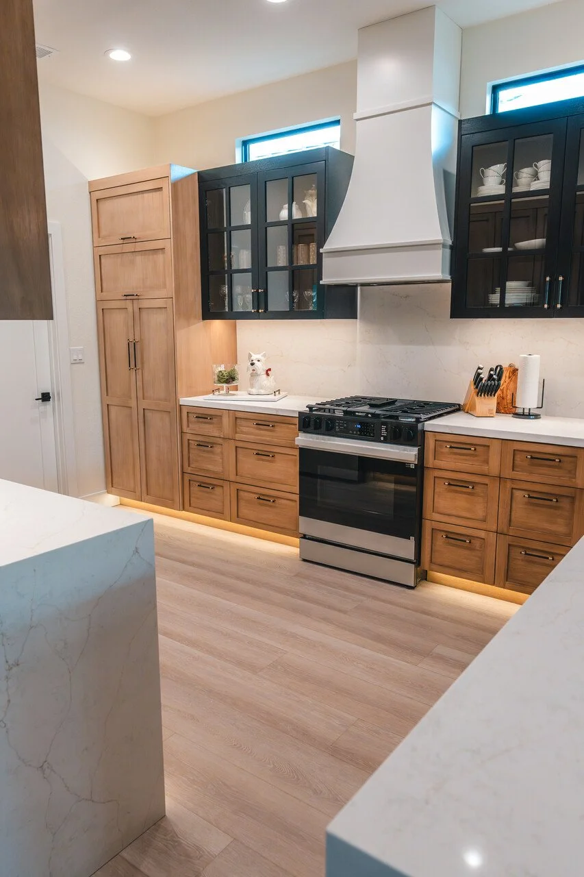 Modern kitchen with wood and black cabinets, a stainless steel stove, and white marble countertops. Decor includes a small llama figurine and a knife block. Light wood flooring.