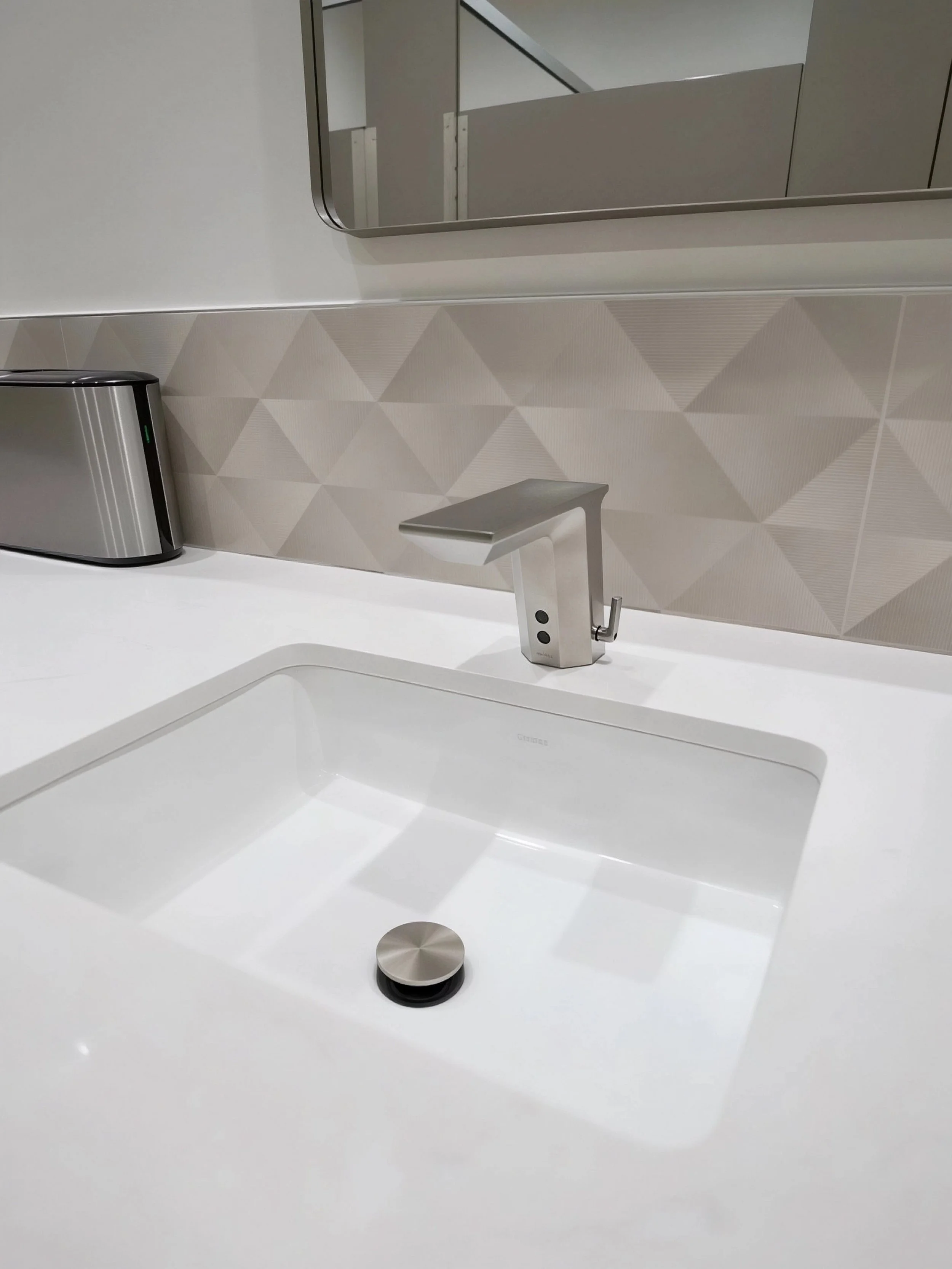 Modern kitchen sink with a sleek silver faucet, a beige geometric tile backsplash, and a reflective mirror above.