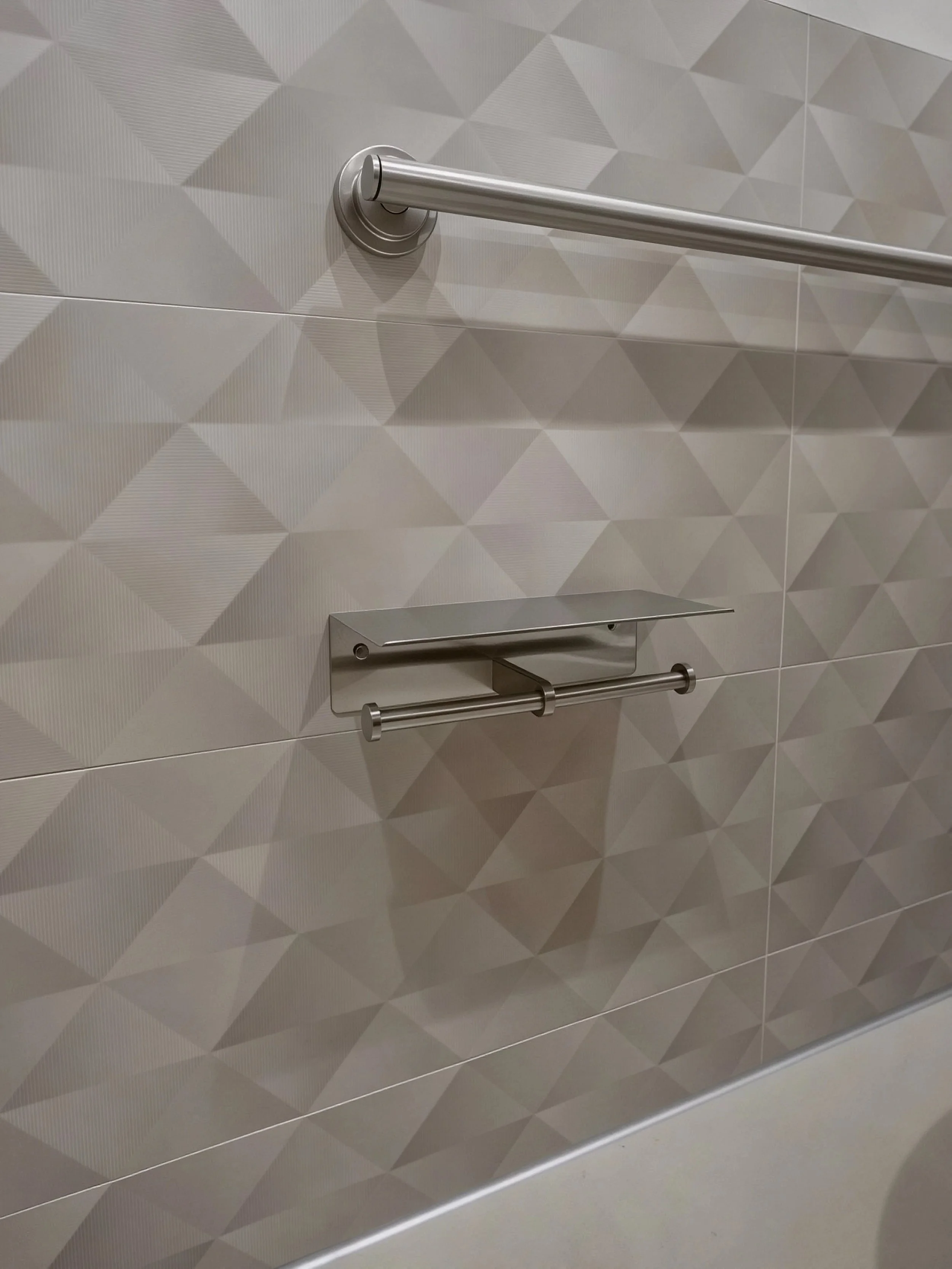 Close-up of a wall-mounted stainless steel paper towel holder and a handrail on a tiled bathroom wall.