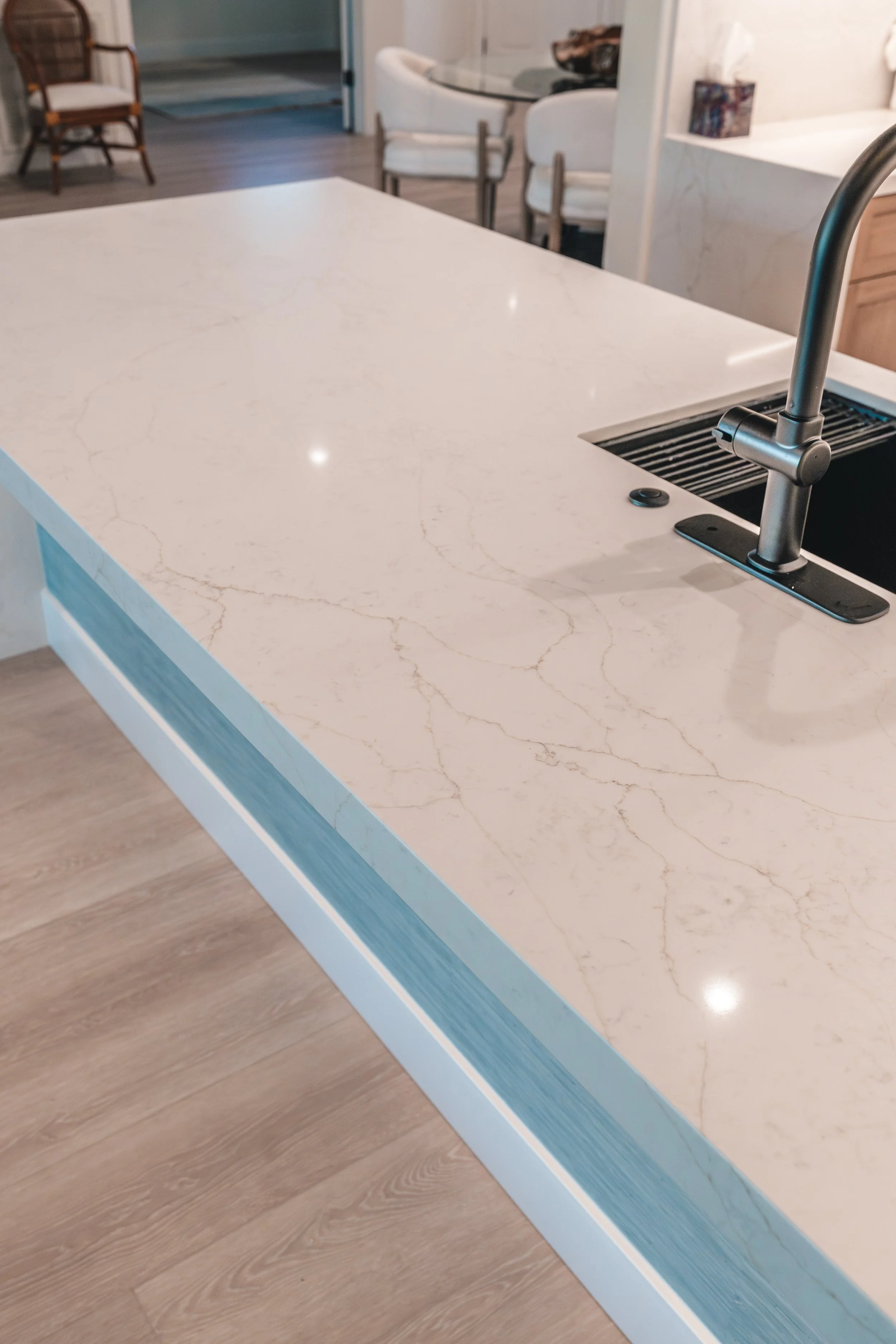 Close-up of a white marble kitchen countertop with subtle gold veining, a modern faucet, and a wooden floor underneath.