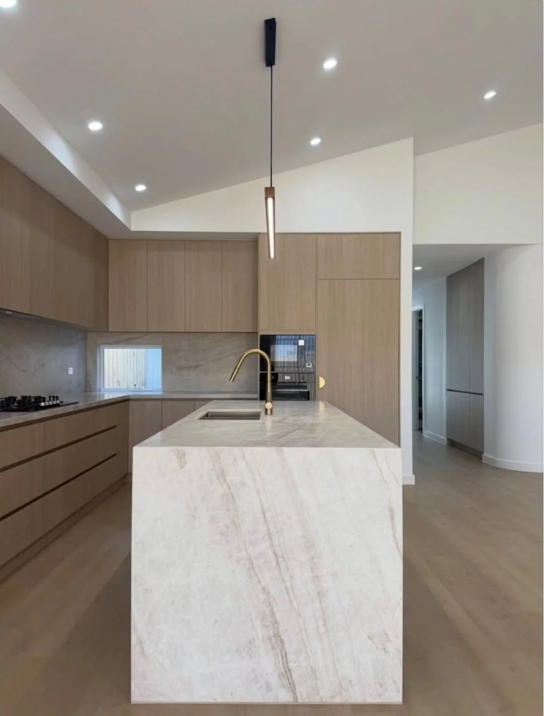 Modern kitchen with a marble island, wooden cabinets, and minimalist lighting.