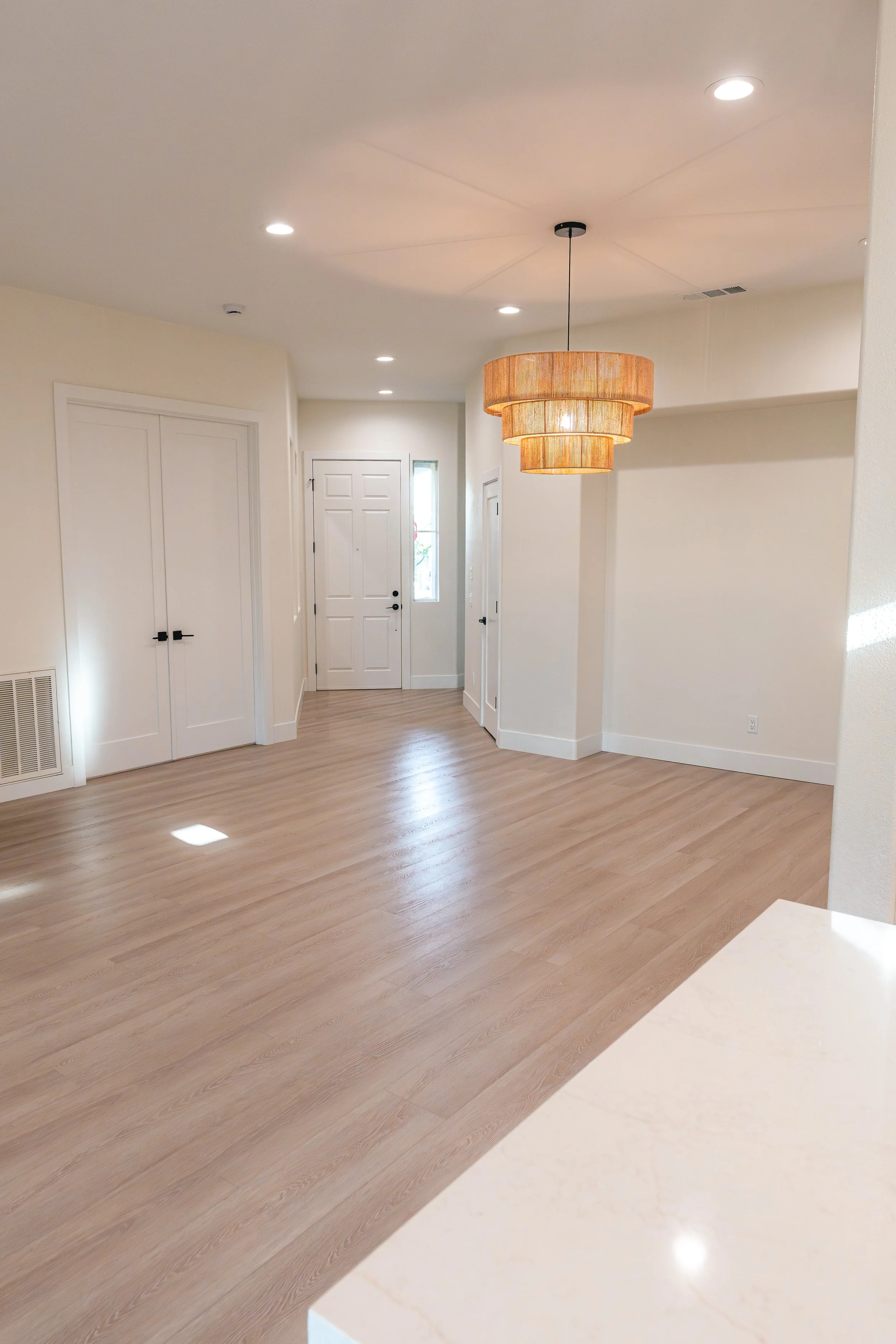 Empty room with light wood flooring, white walls, a modern chandelier, and a white front door with a small window next to it.