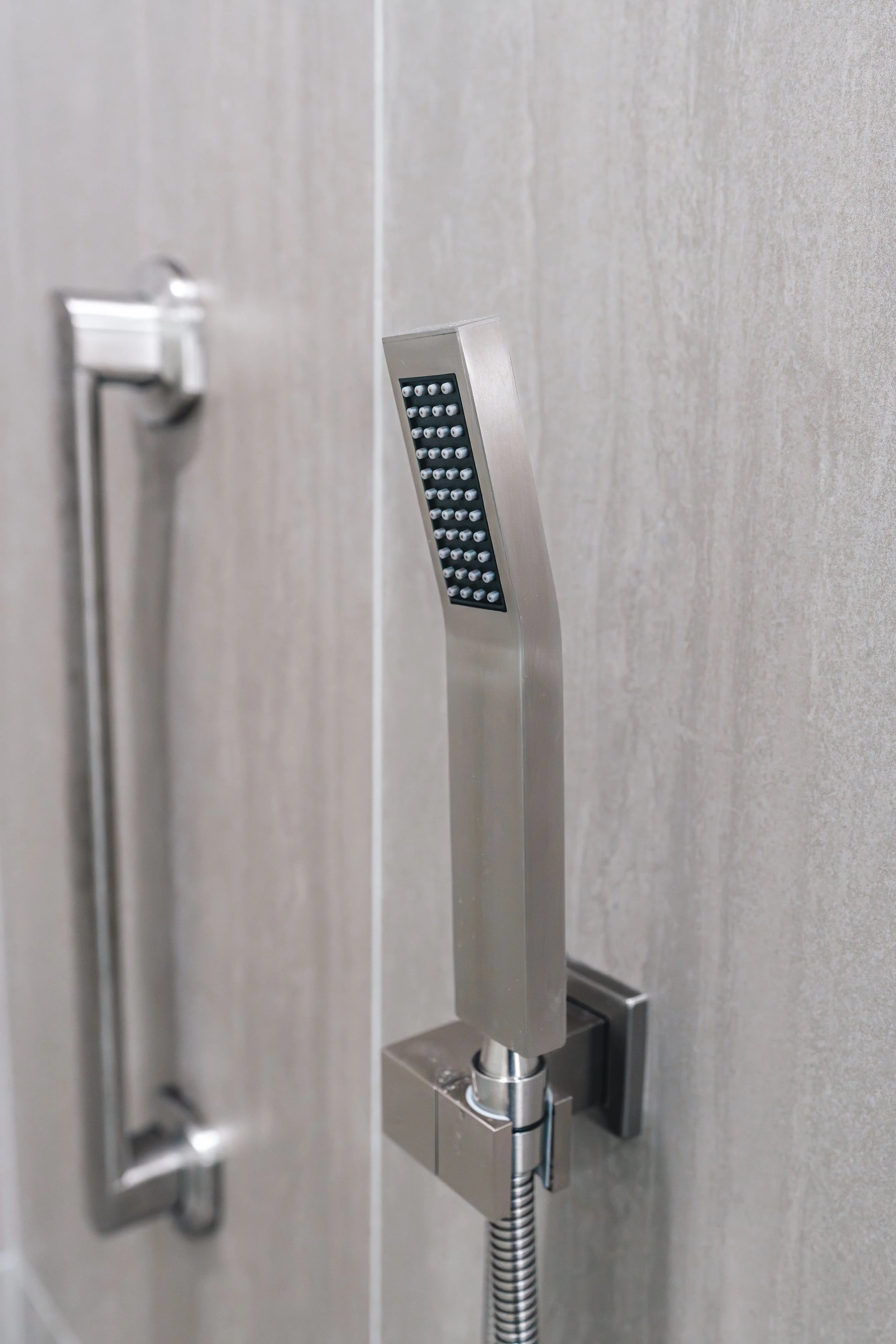 A modern metal shower head with multiple spray nozzles mounted on a beige tiled wall.