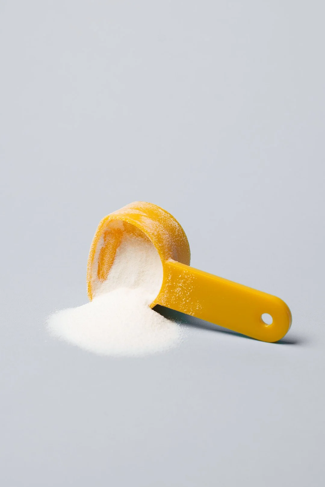 A yellow plastic scoop filled with ONE Stride Pet supplement powder, resting on a light gray surface.
