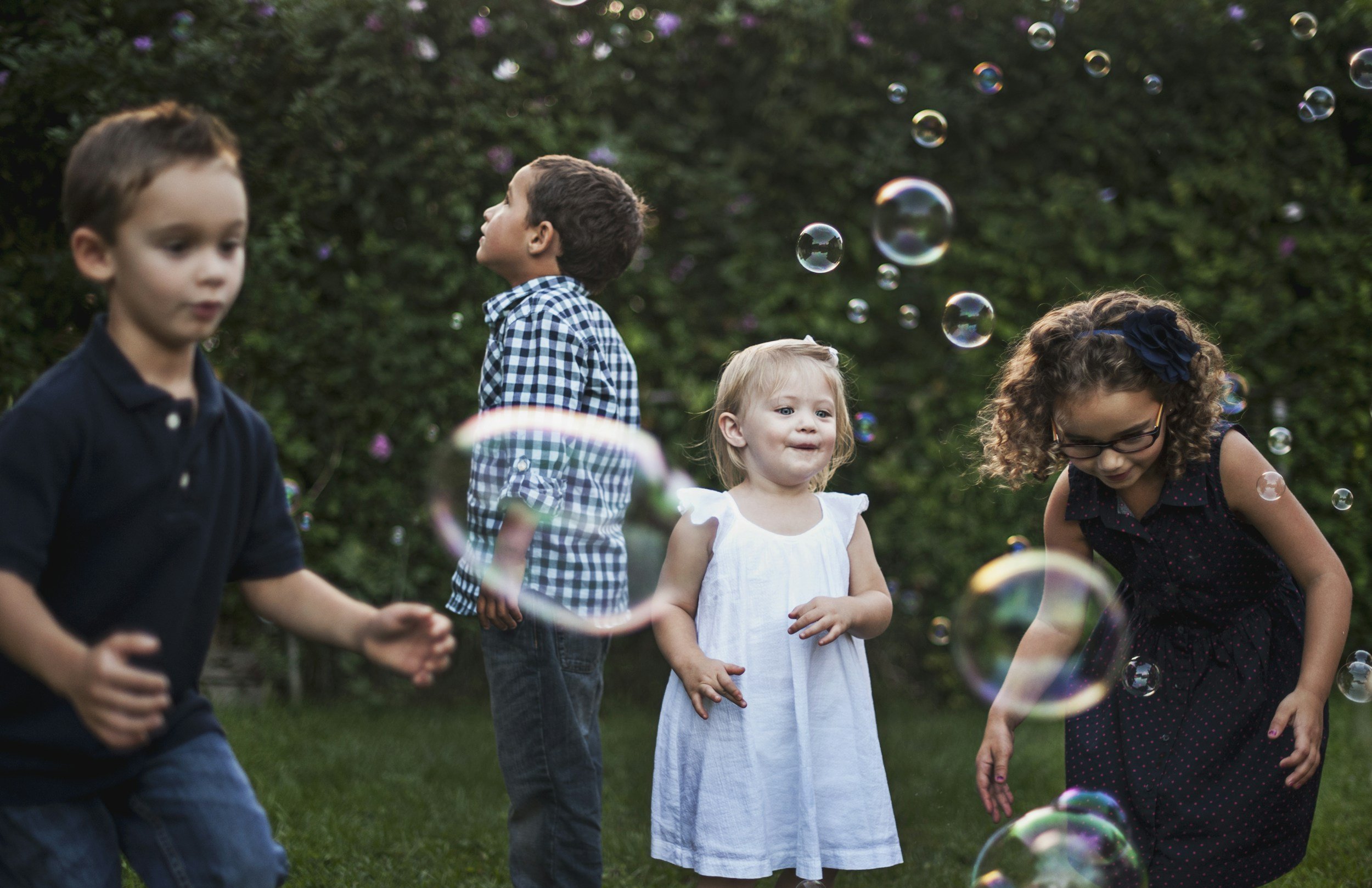 Children playing with bubbles outdoors in a lush green area.