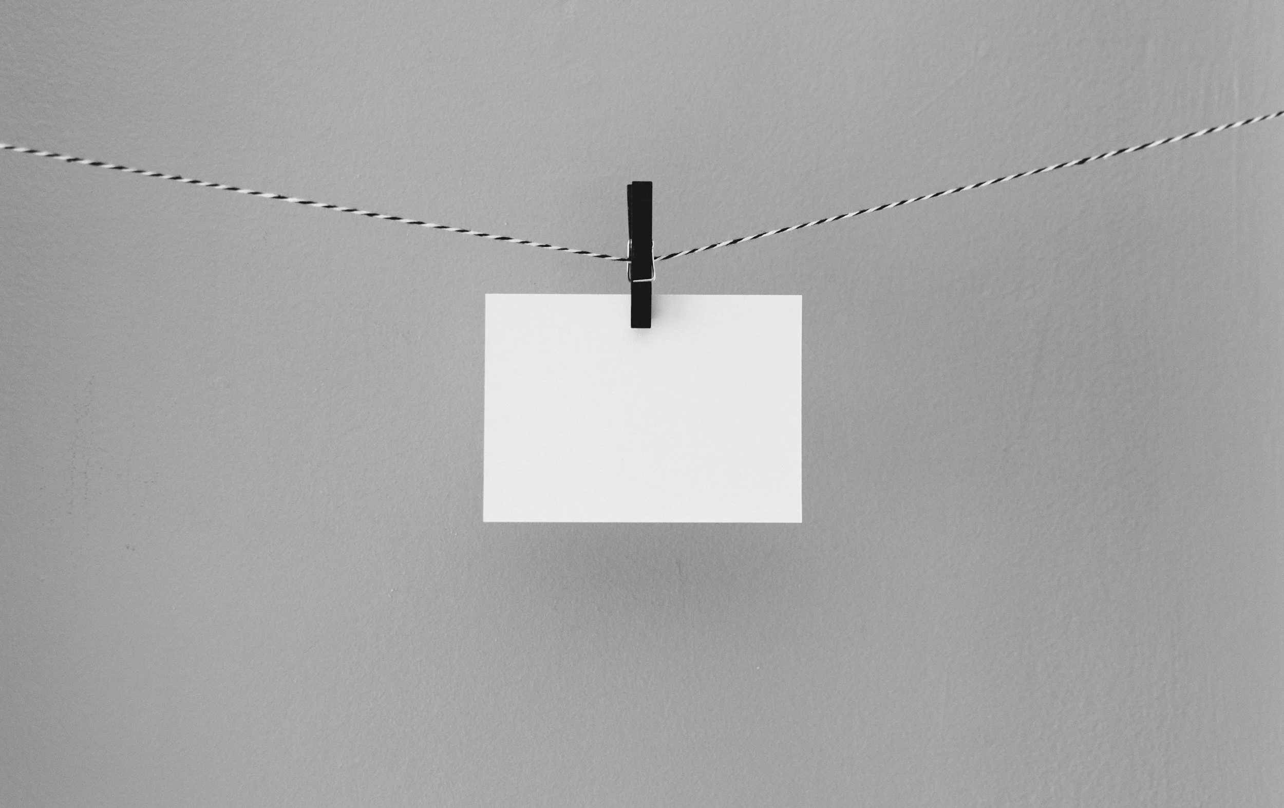 A black clothespin attached to a string with a blank white card hanging from it on a gray wall.