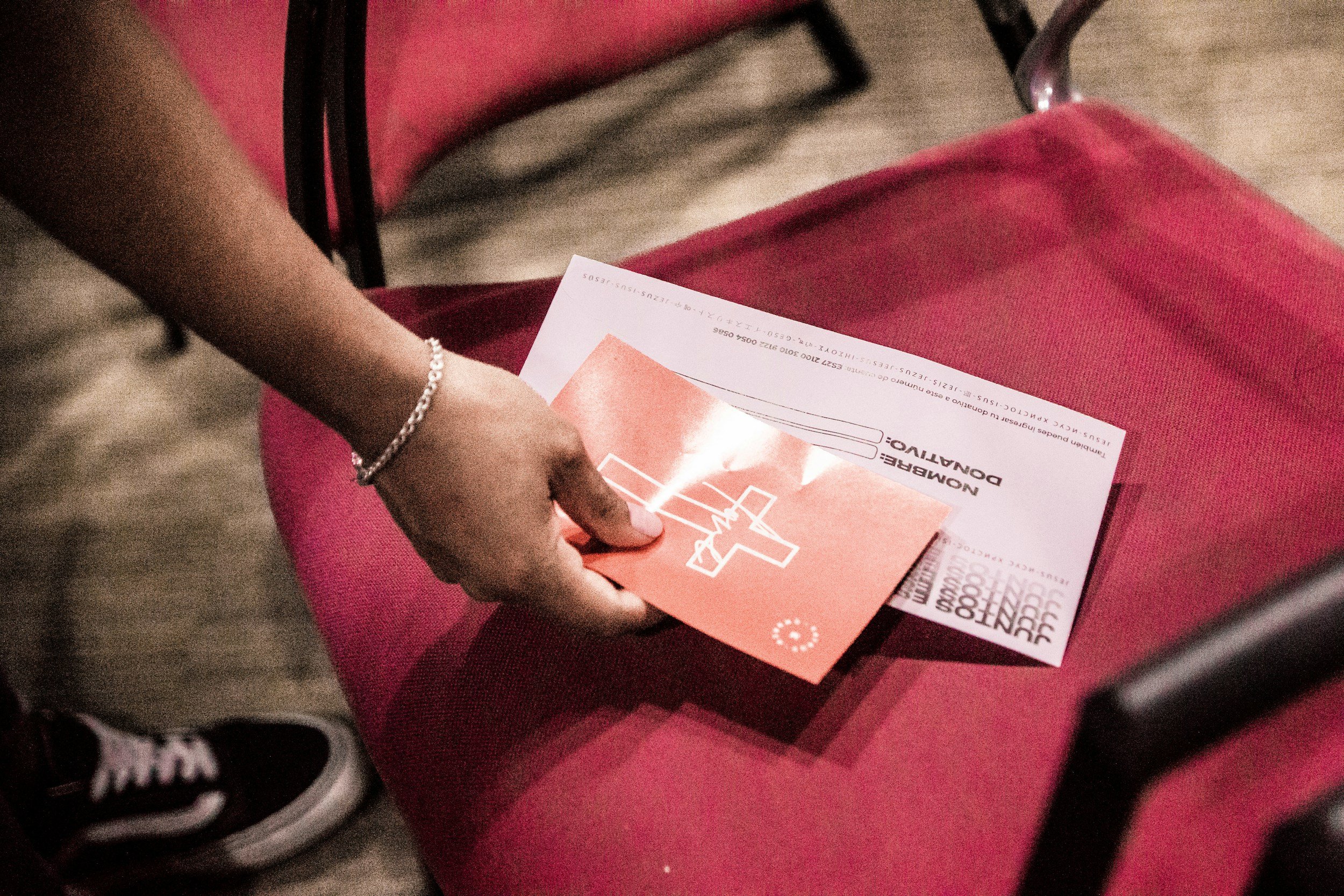 Person holding a Paper in a red folder sitting on a red cushioned seat.