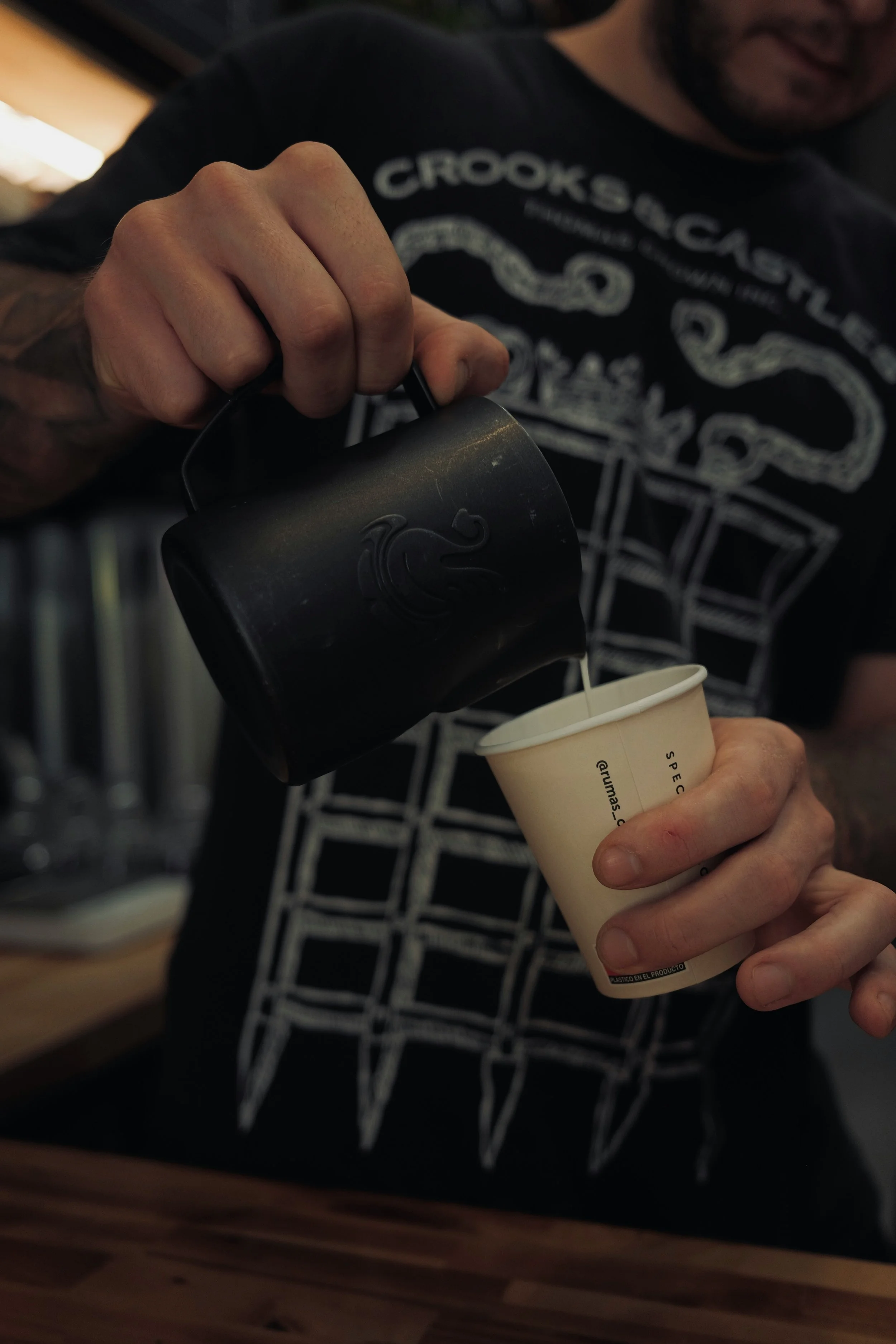 A man pouring coffee from a black mug into a paper cup.