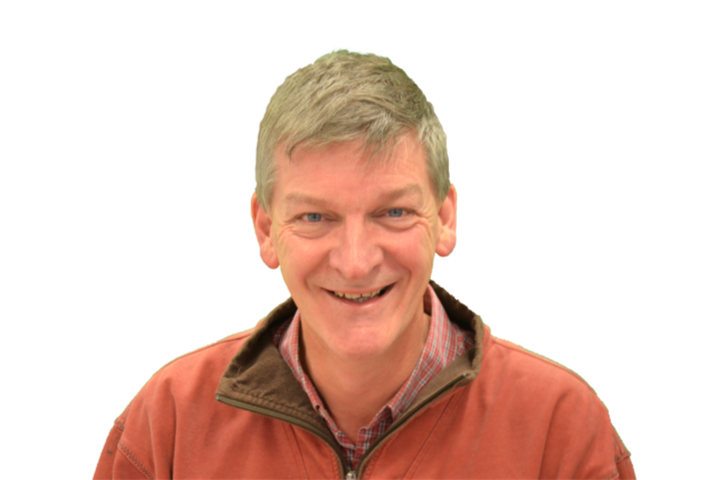 A middle-aged man with gray hair smiling, wearing a red jacket over a plaid shirt, against a white background.