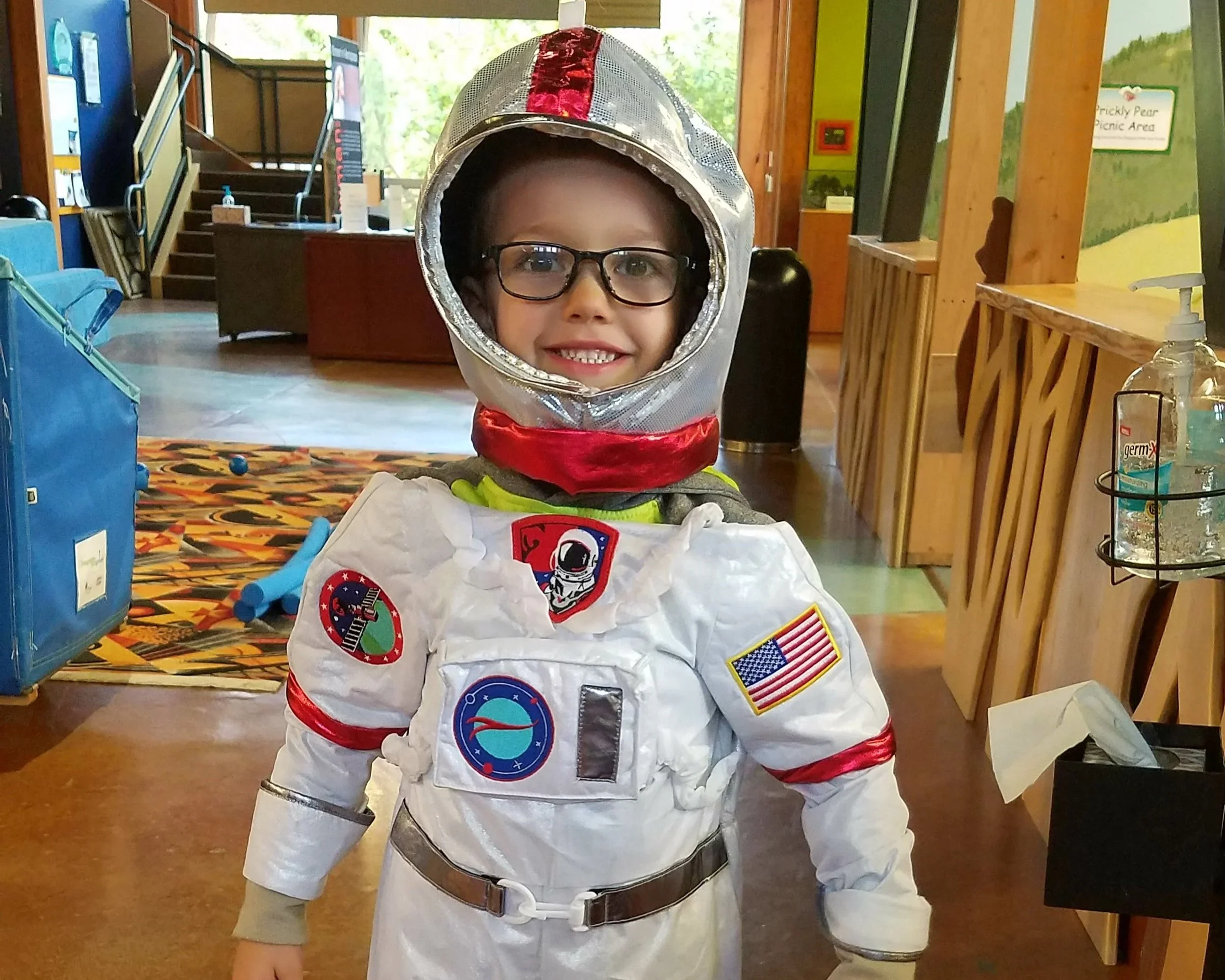 Young child smiling and wearing a NASA astronaut costume in an indoor setting.