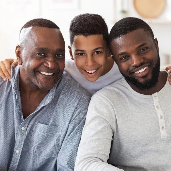 Three smiling men of different ages, sitting close together indoors.