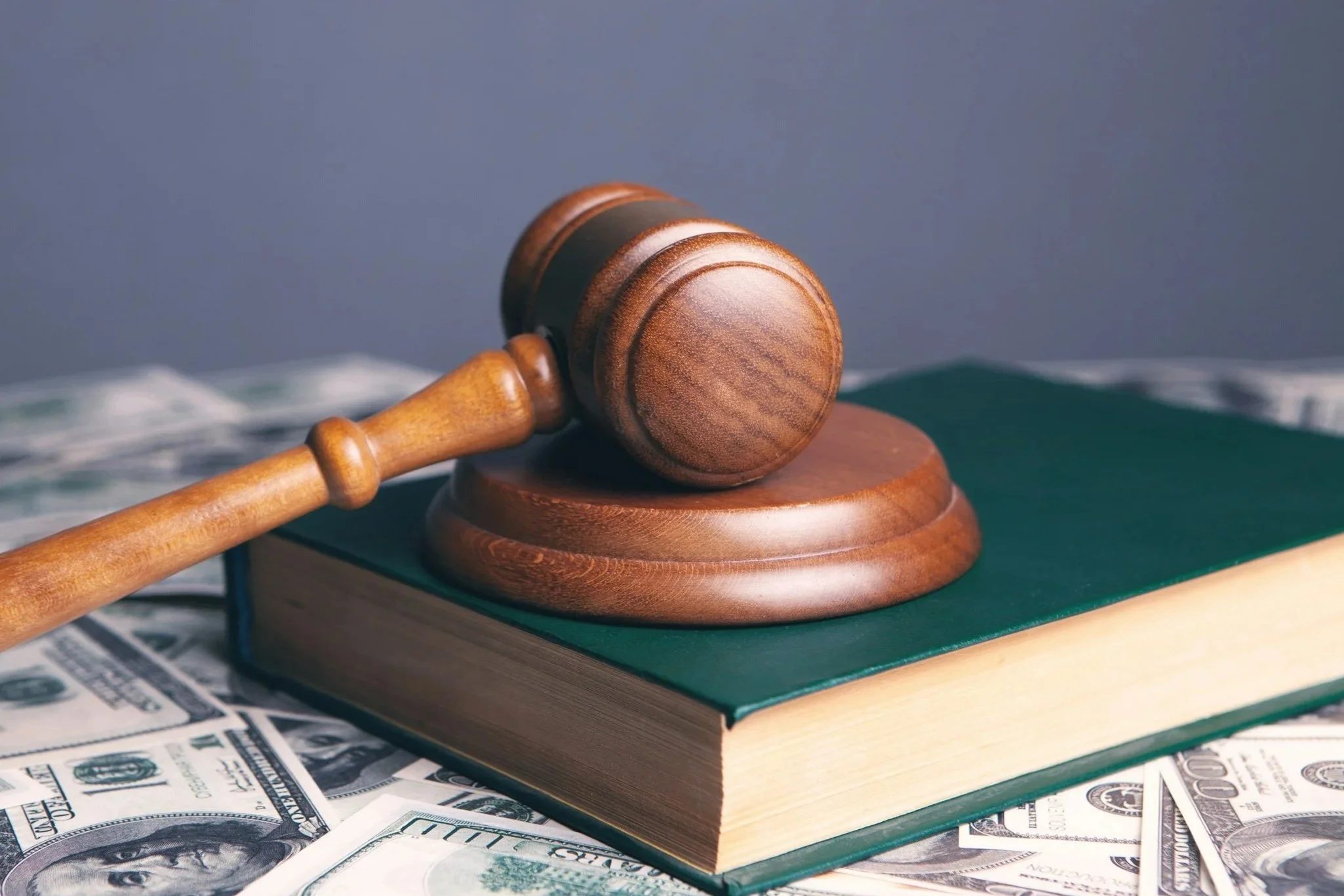 A wooden gavel resting on a sound block placed on top of a green-bound law book.