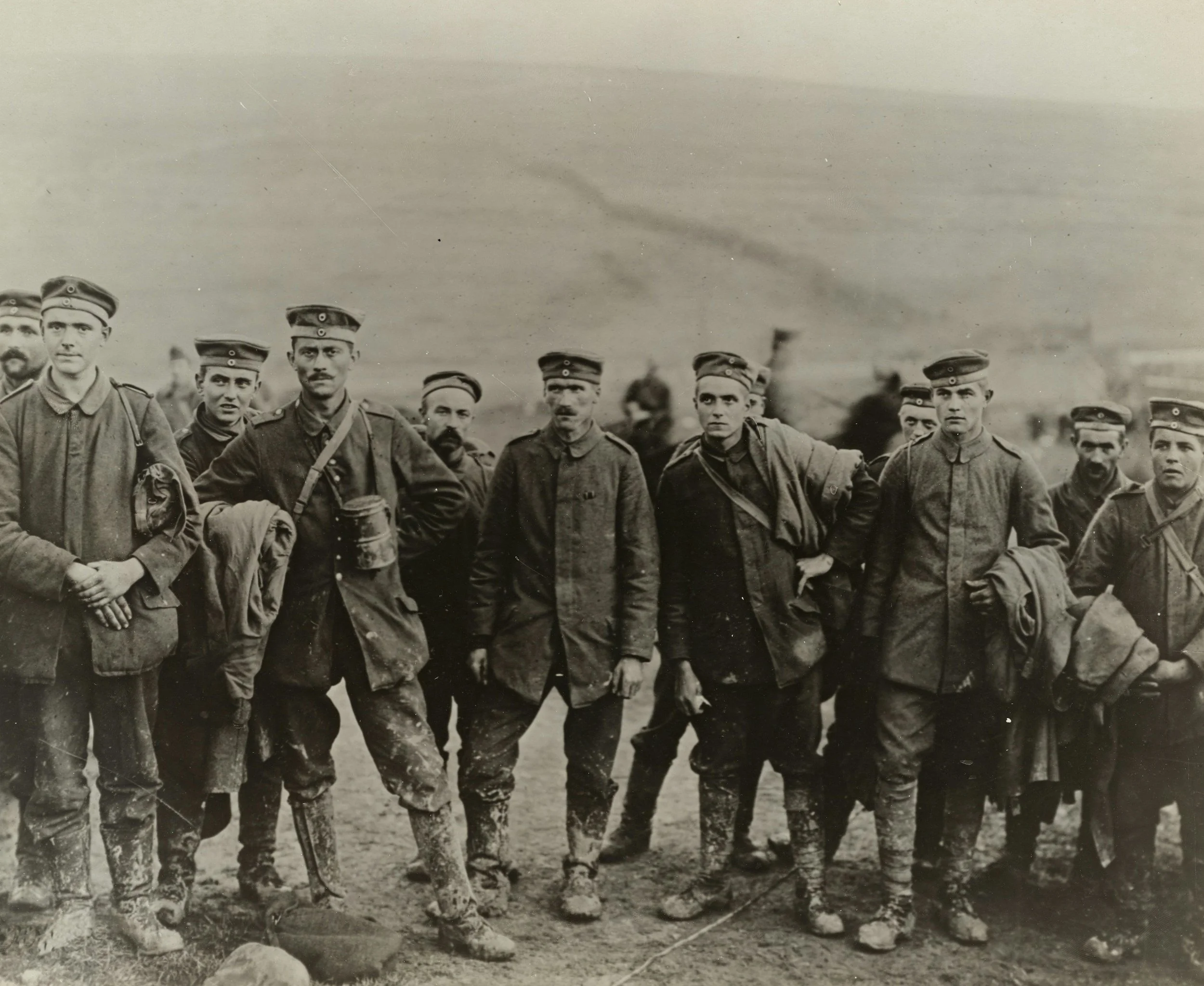 Black and white photo of a group of soldiers in uniform standing outdoors, some with hands on hips, with a hazy background and desolate landscape.