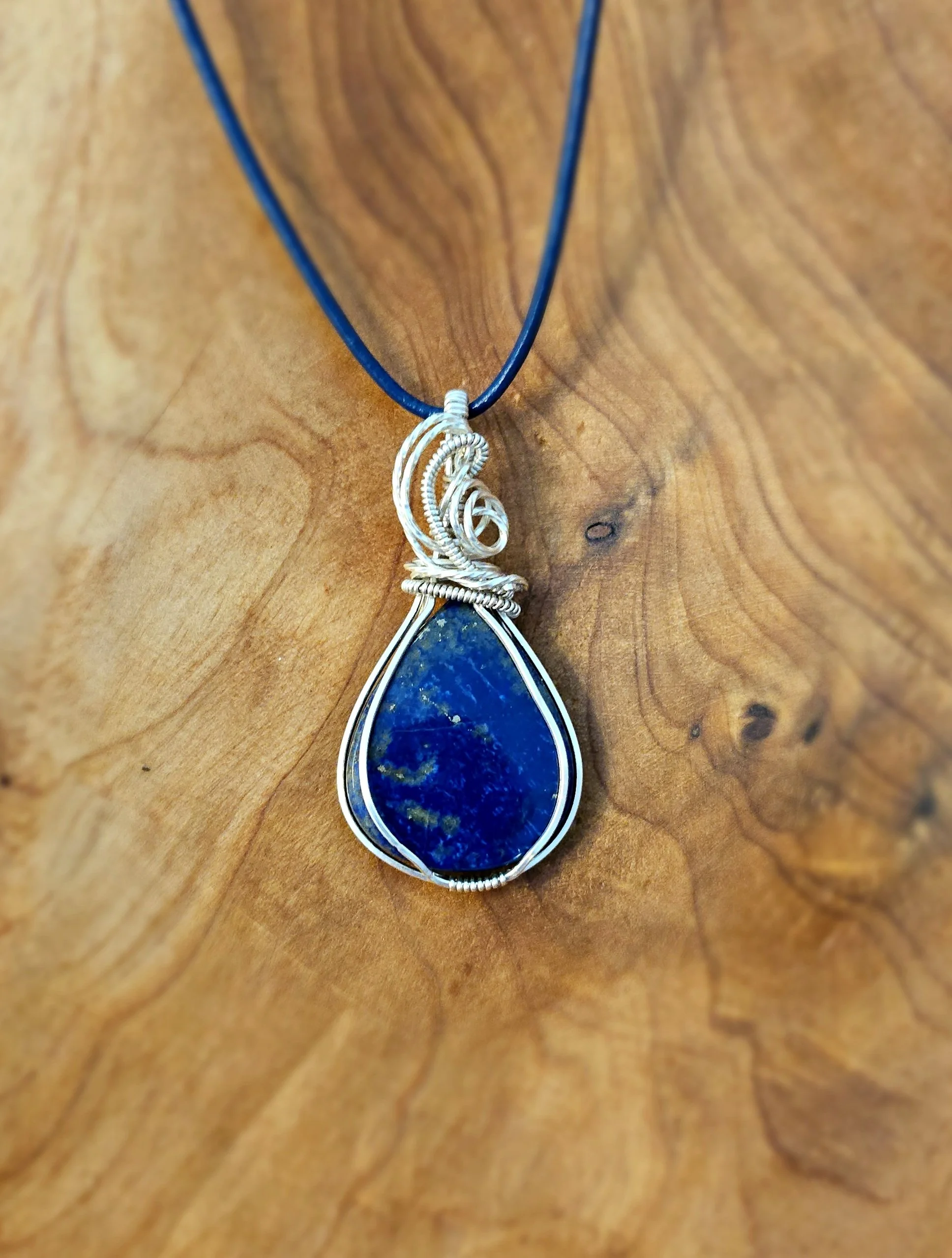 Silver wire-wrapped necklace with a large blue teardrop-shaped gemstone on a wooden surface.
