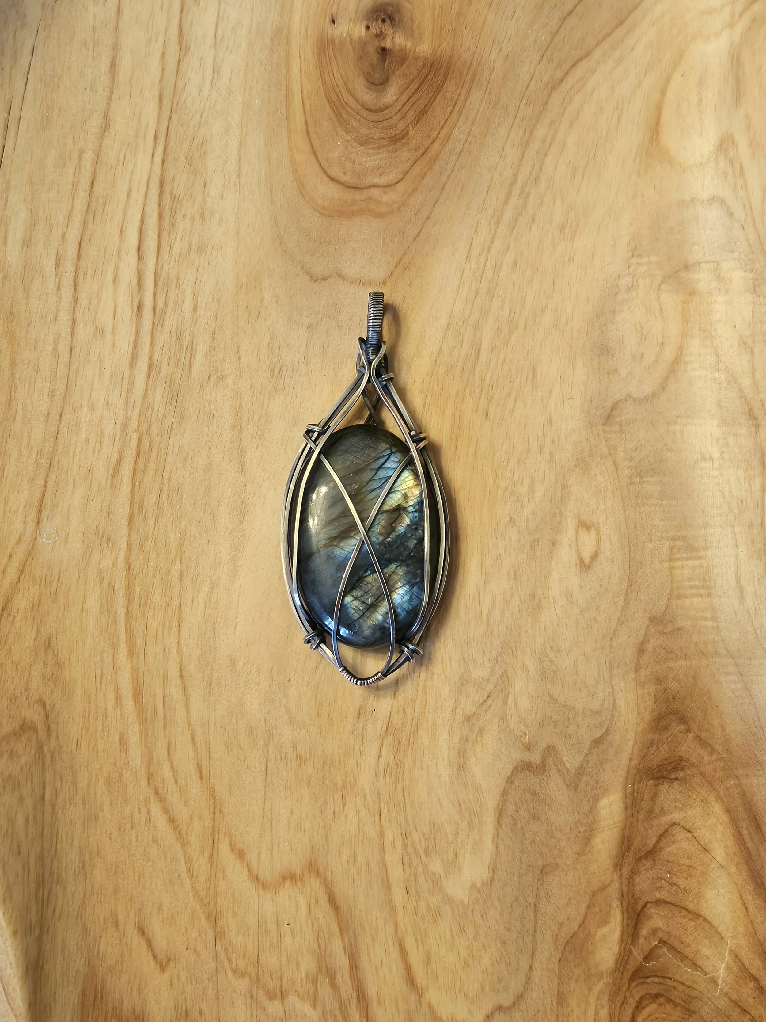 A pendant with a large labradorite gemstone wrapped in wire on a wooden surface.