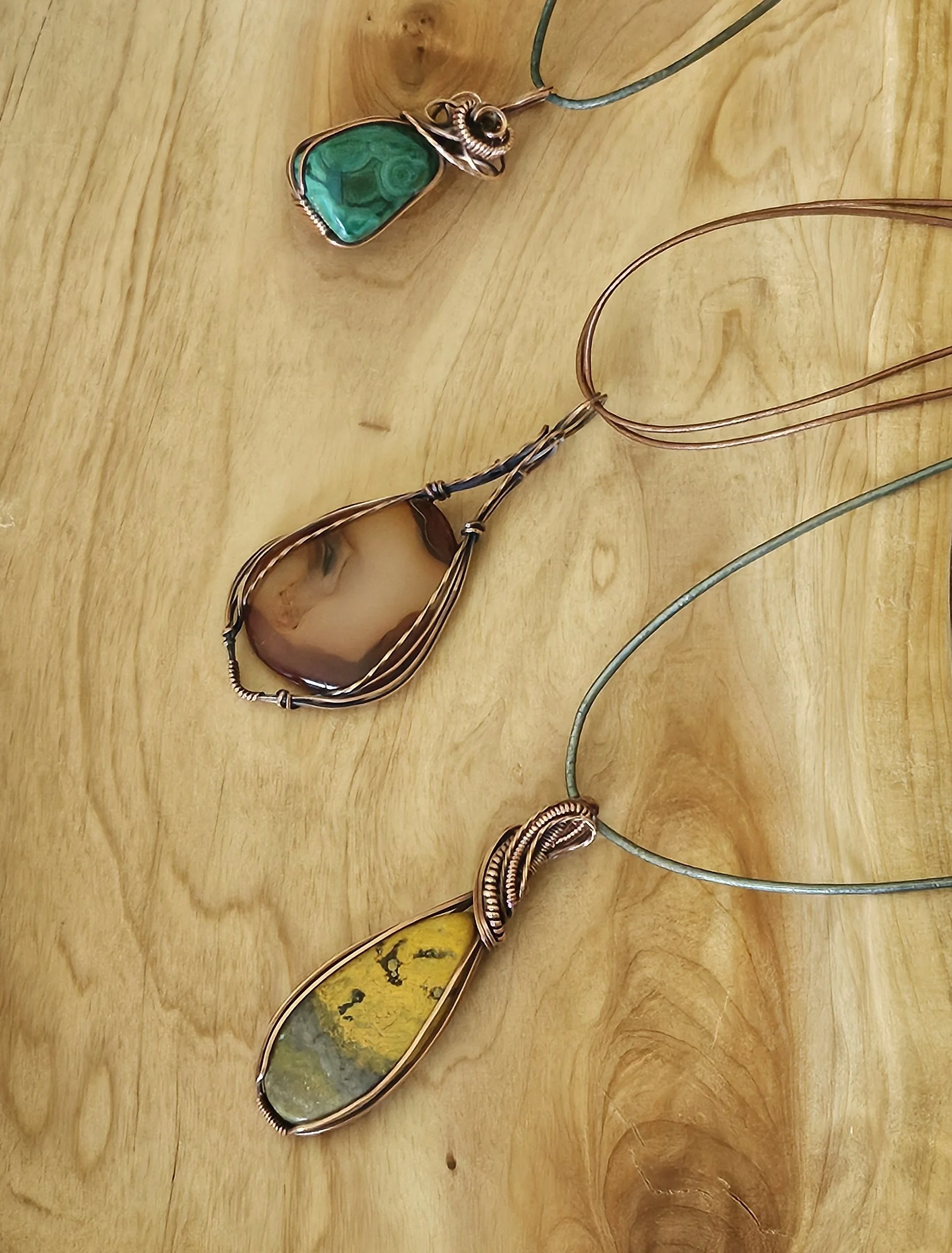 Three wire wrapped stone pendants on metal chains placed on a wooden surface.
