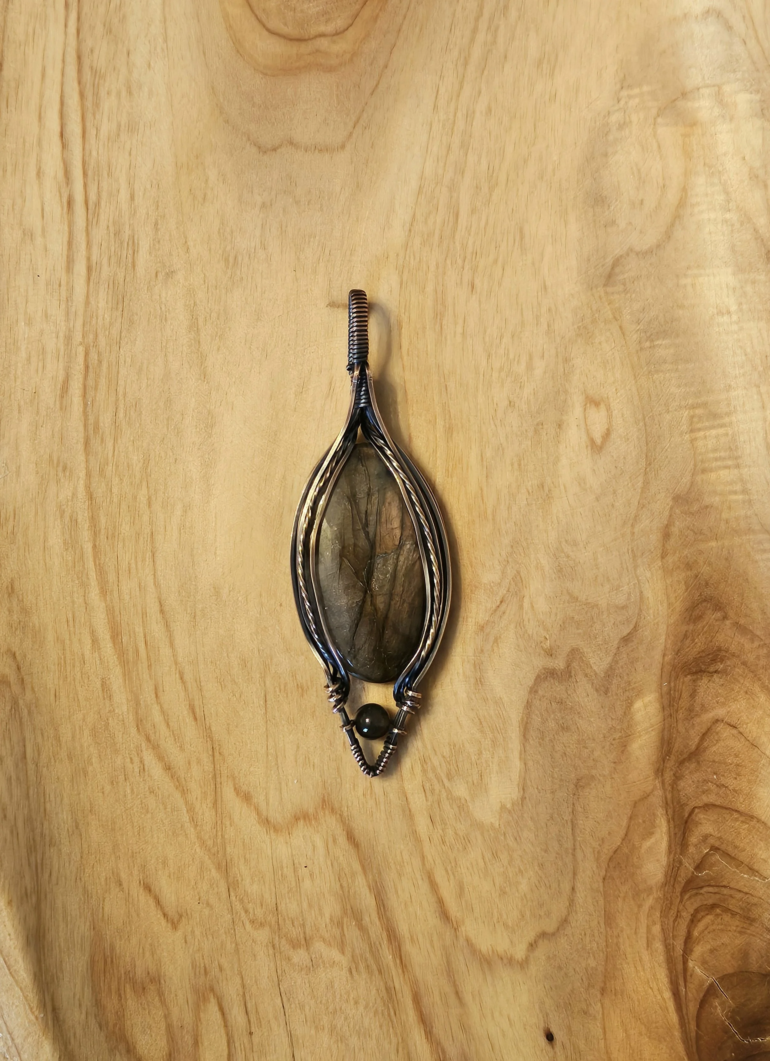 Handmade wire jewelry holder with a large stone inside, placed on a wooden surface.