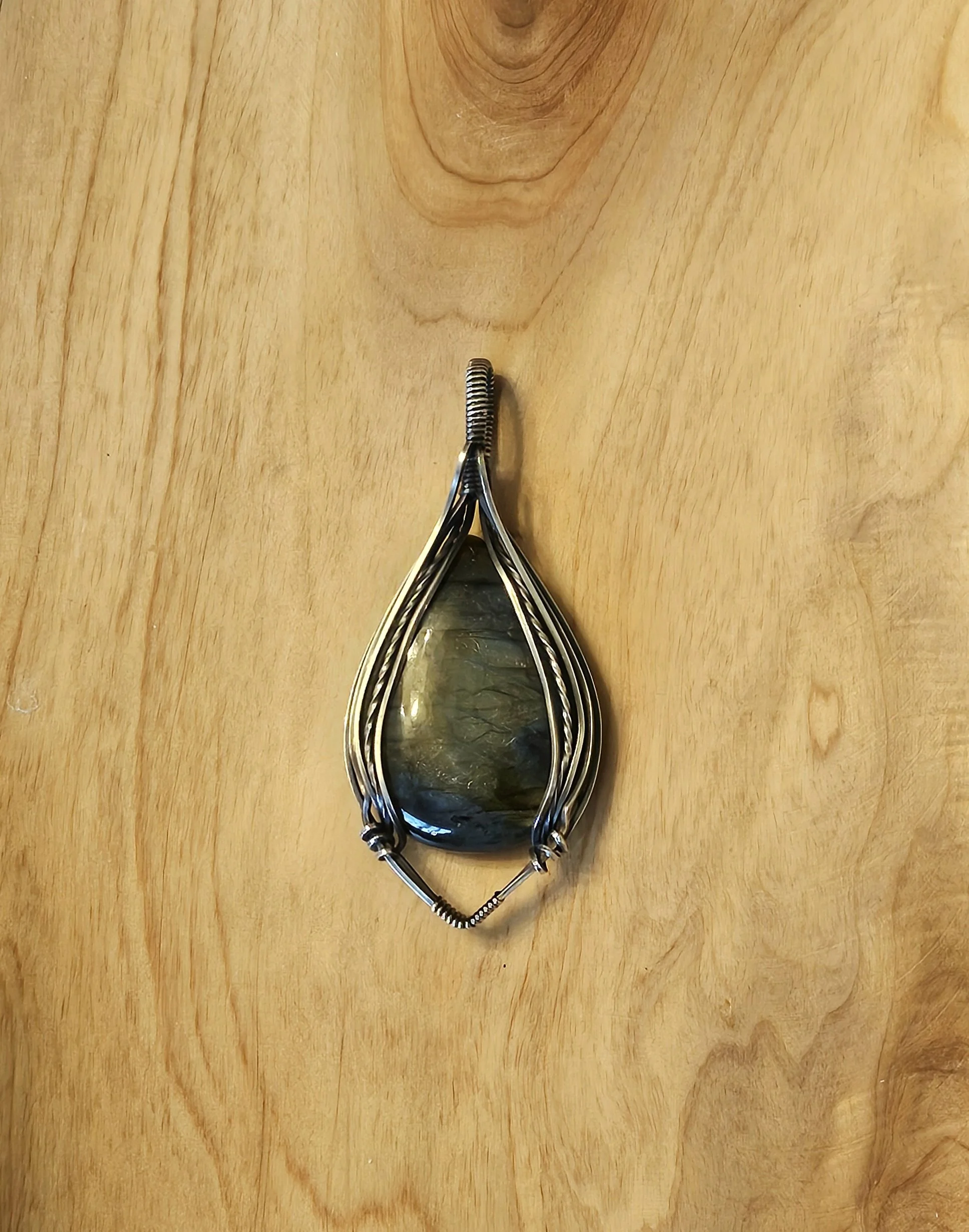 Silver wire pendant with a large, polished, dark greenish-black stone on a wooden surface.
