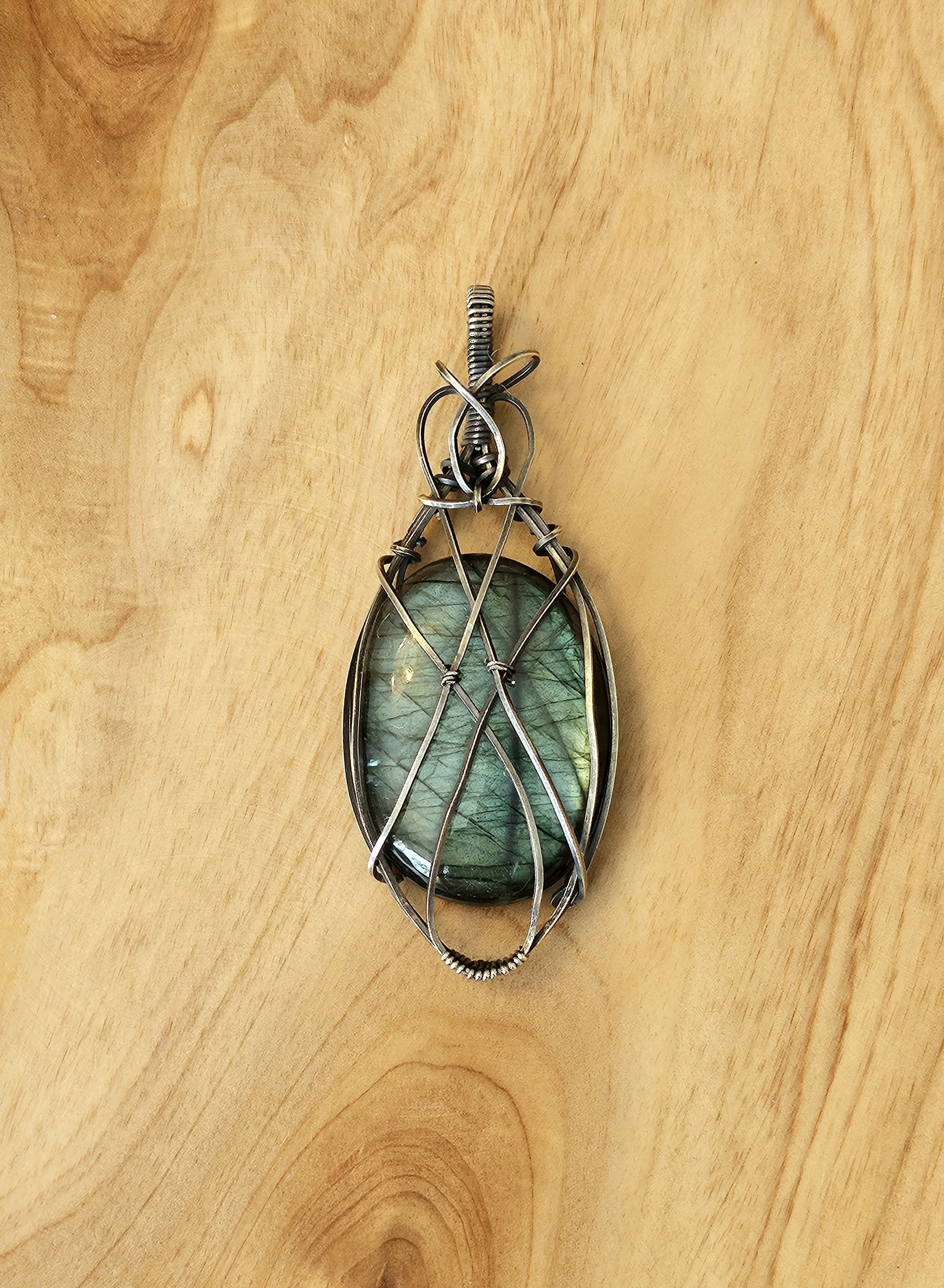 A pendant featuring a large green gemstone wrapped in silver wire, hanging from a silver chain.