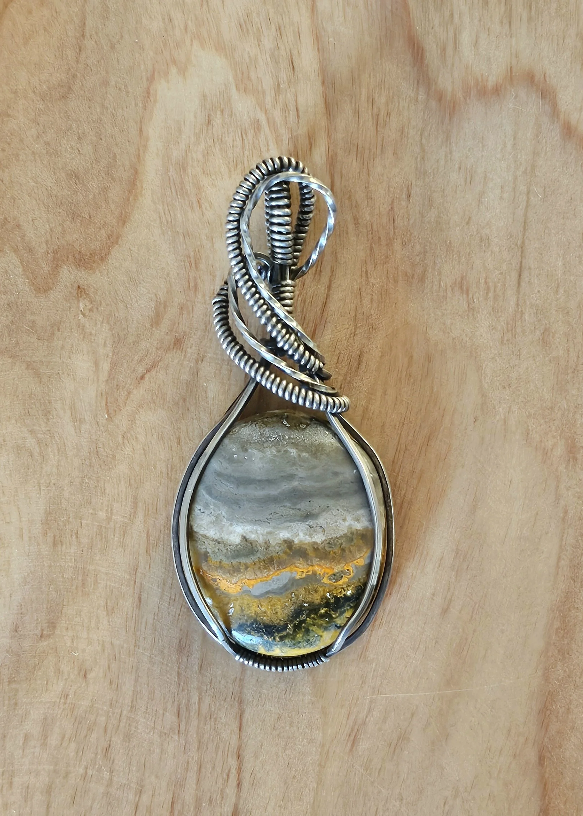 Pendant made of a polished stone with yellow, gray, and white patterns, wrapped in twisted silver wire.