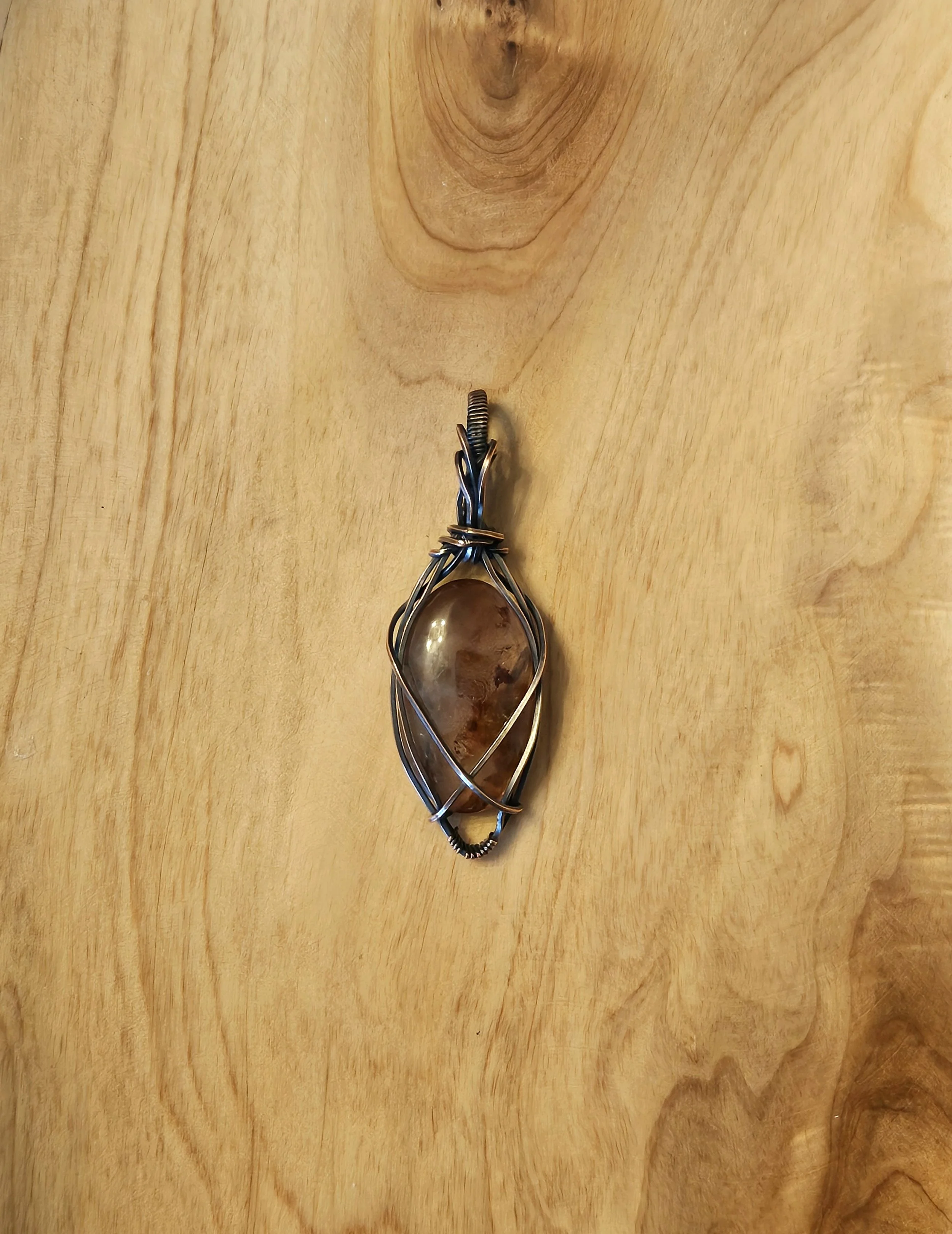 Wire-wrapped pendant with a polished brown stone on a wooden surface.