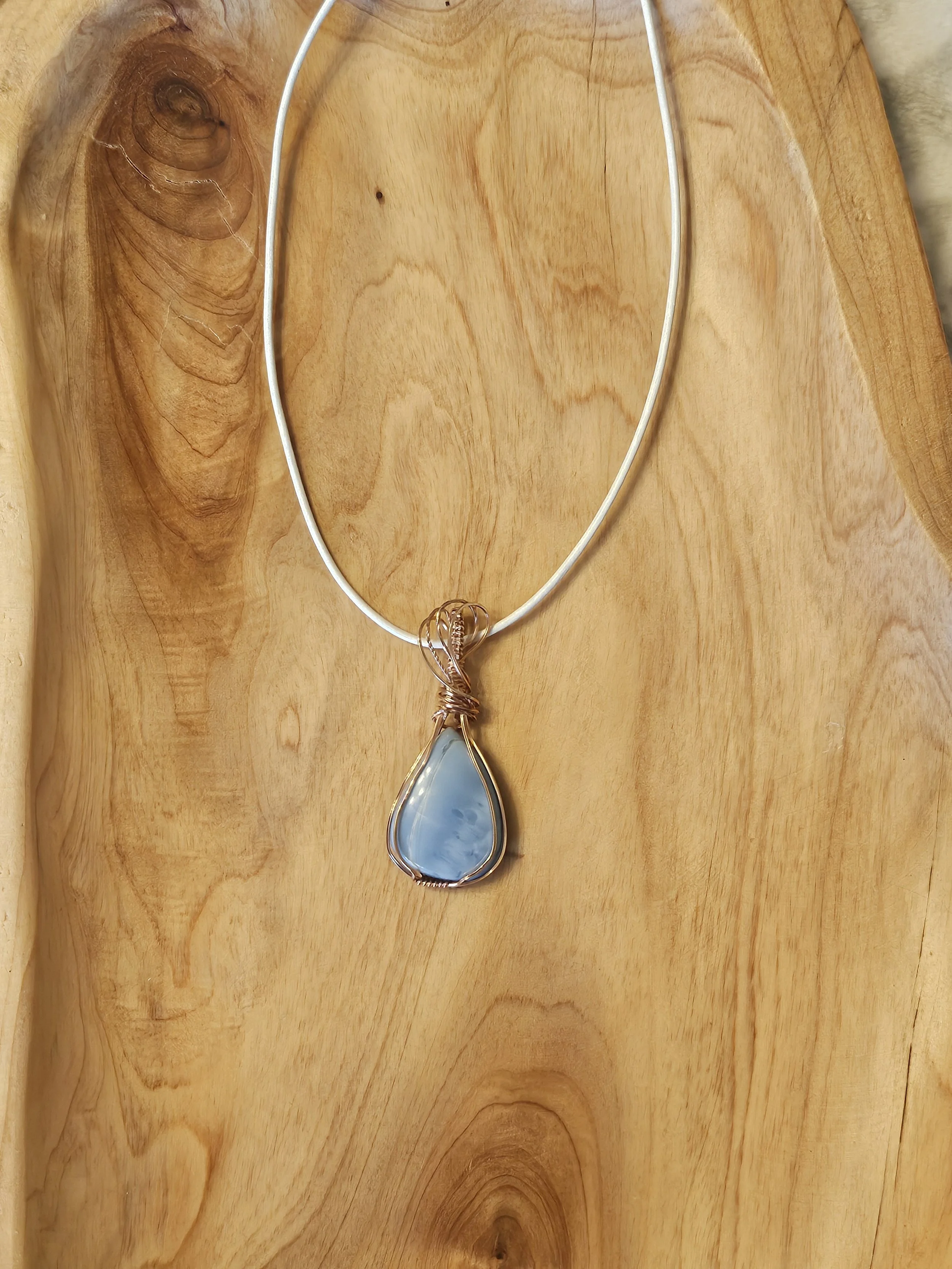 Silver necklace with a large teardrop-shaped blue gemstone pendant on a wooden surface.