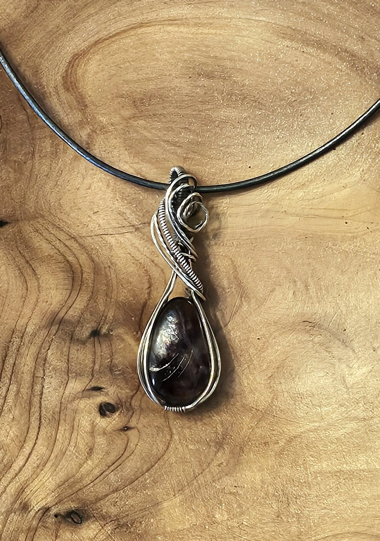 Silver necklace with a large black stone pendant worn on a wooden surface.