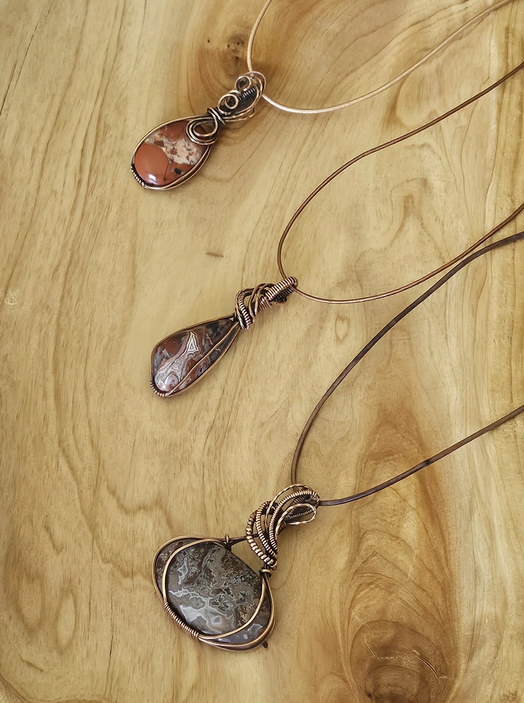 Three necklaces with large, polished stone pendants wrapped in wire, laid out on a wooden surface.
