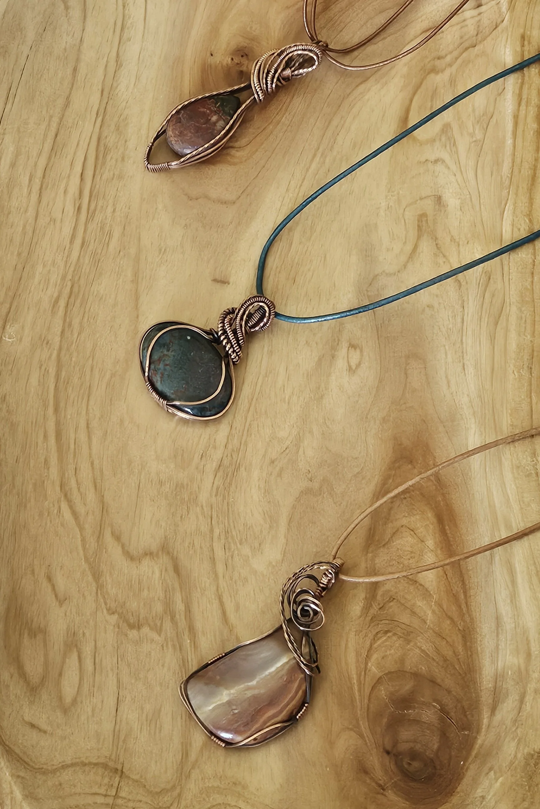 Three wire-wrapped necklaces with large stones on a wooden surface.