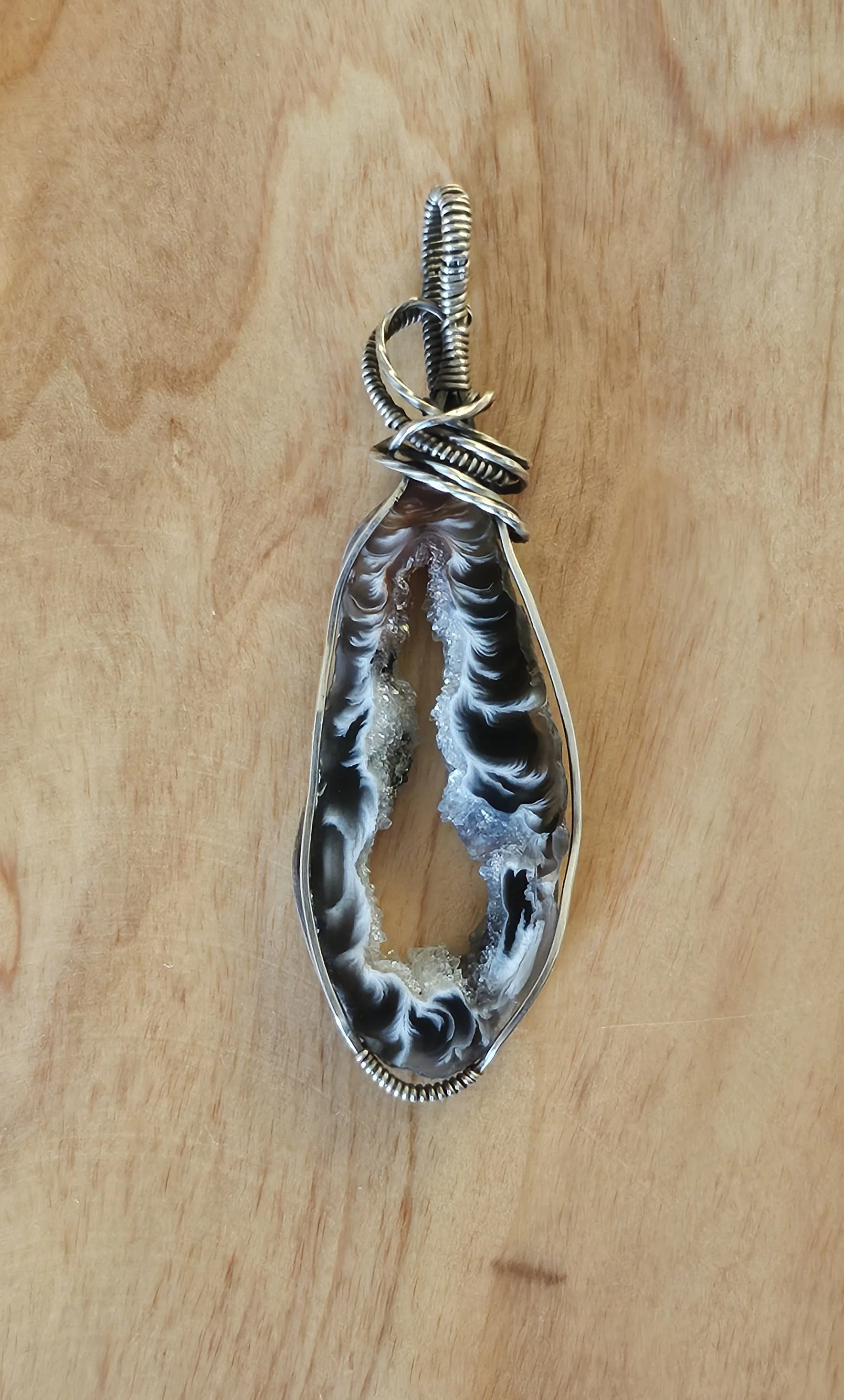 A pendant with a large, oval-shaped, black and white agate stone set in a wire-wrapped silver setting on a wooden surface.