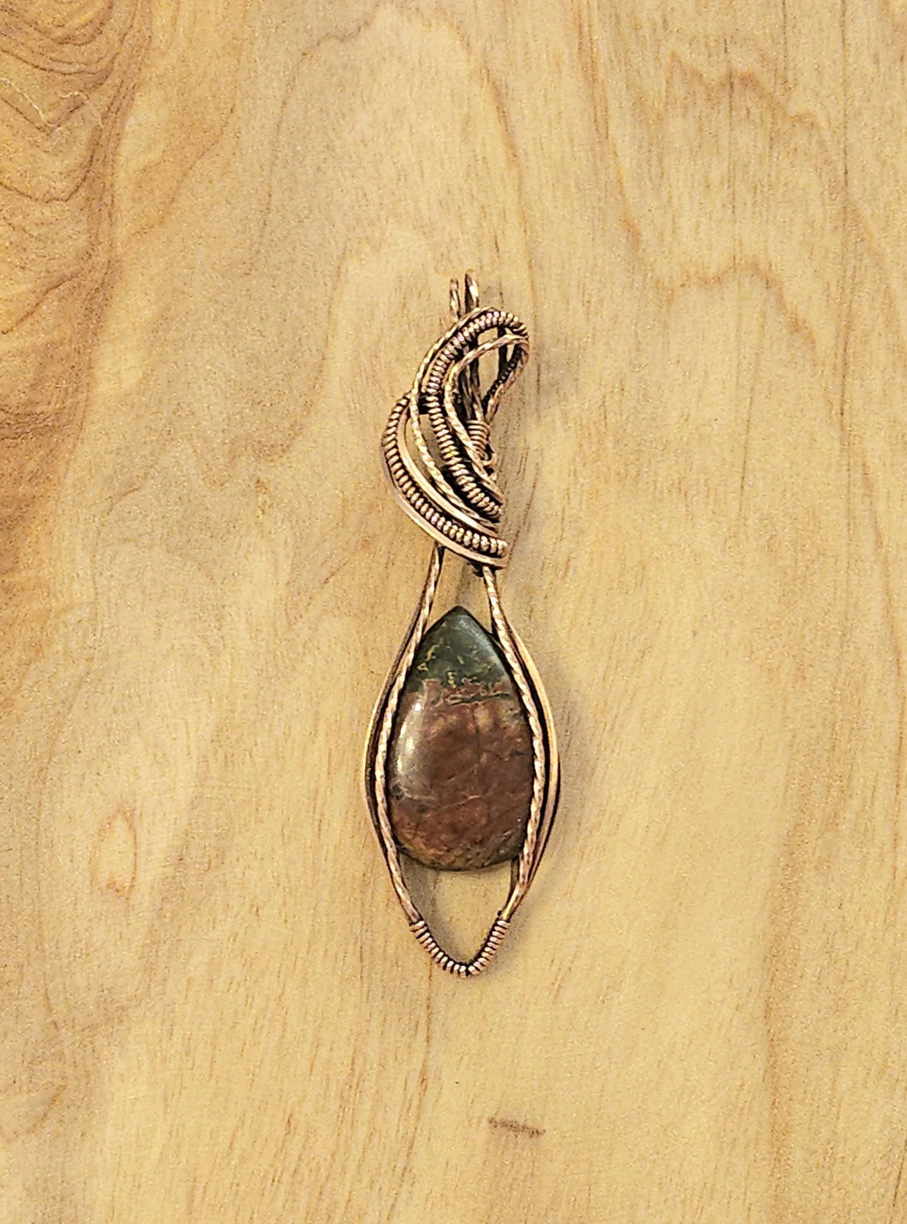 A decorative pendant with a large, polished stone set in a gold-toned wire frame, featuring intricate wire details at the top.