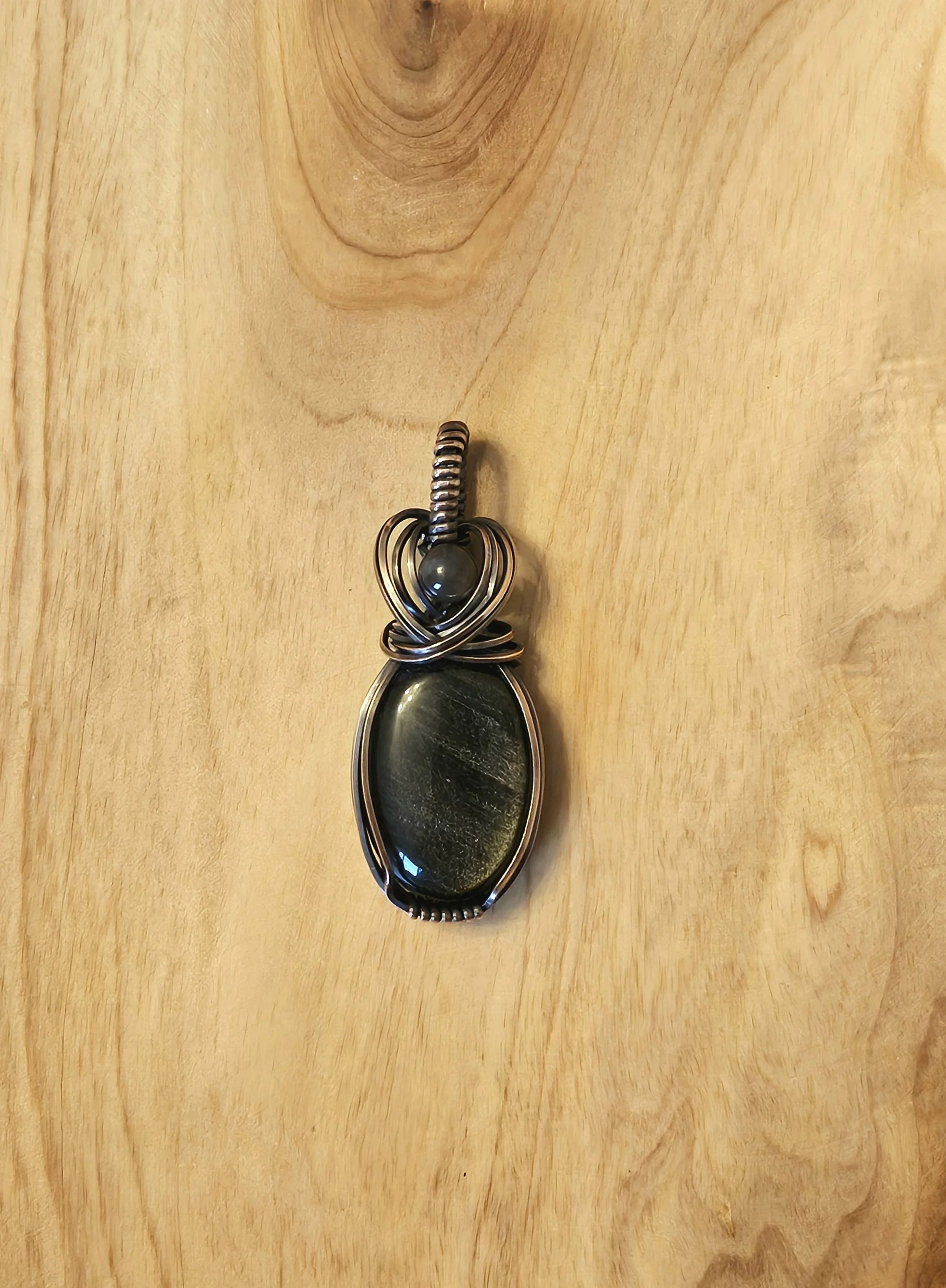 A pendant with a large black stone wrapped in metal wire, hanging on a plain wooden surface.