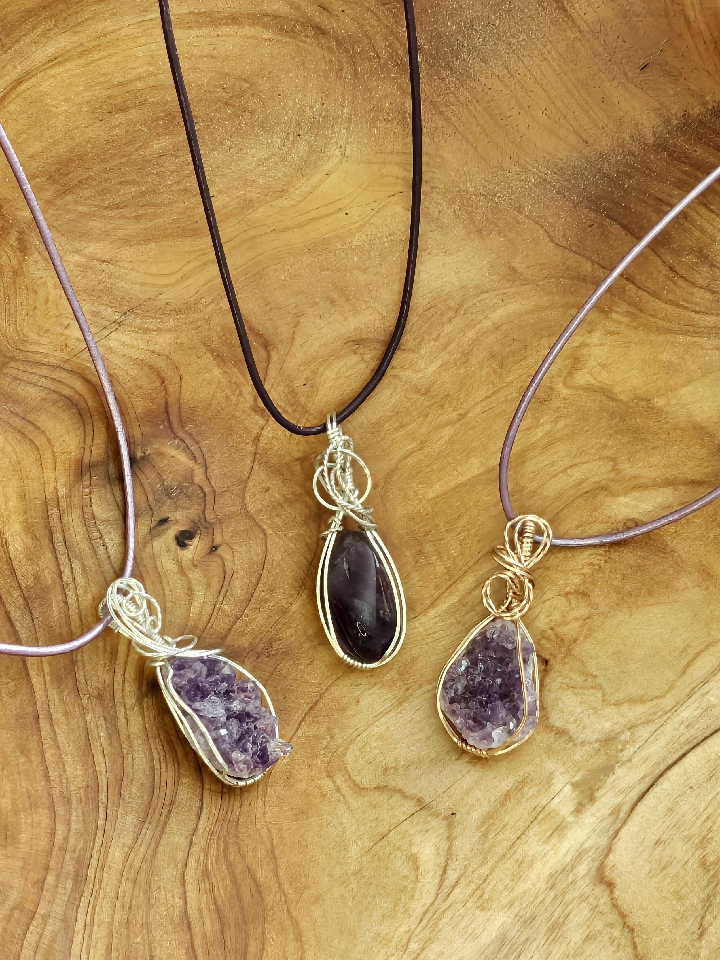 Three wire-wrapped gemstone necklaces on a wooden surface, each with a different stone and chain color.