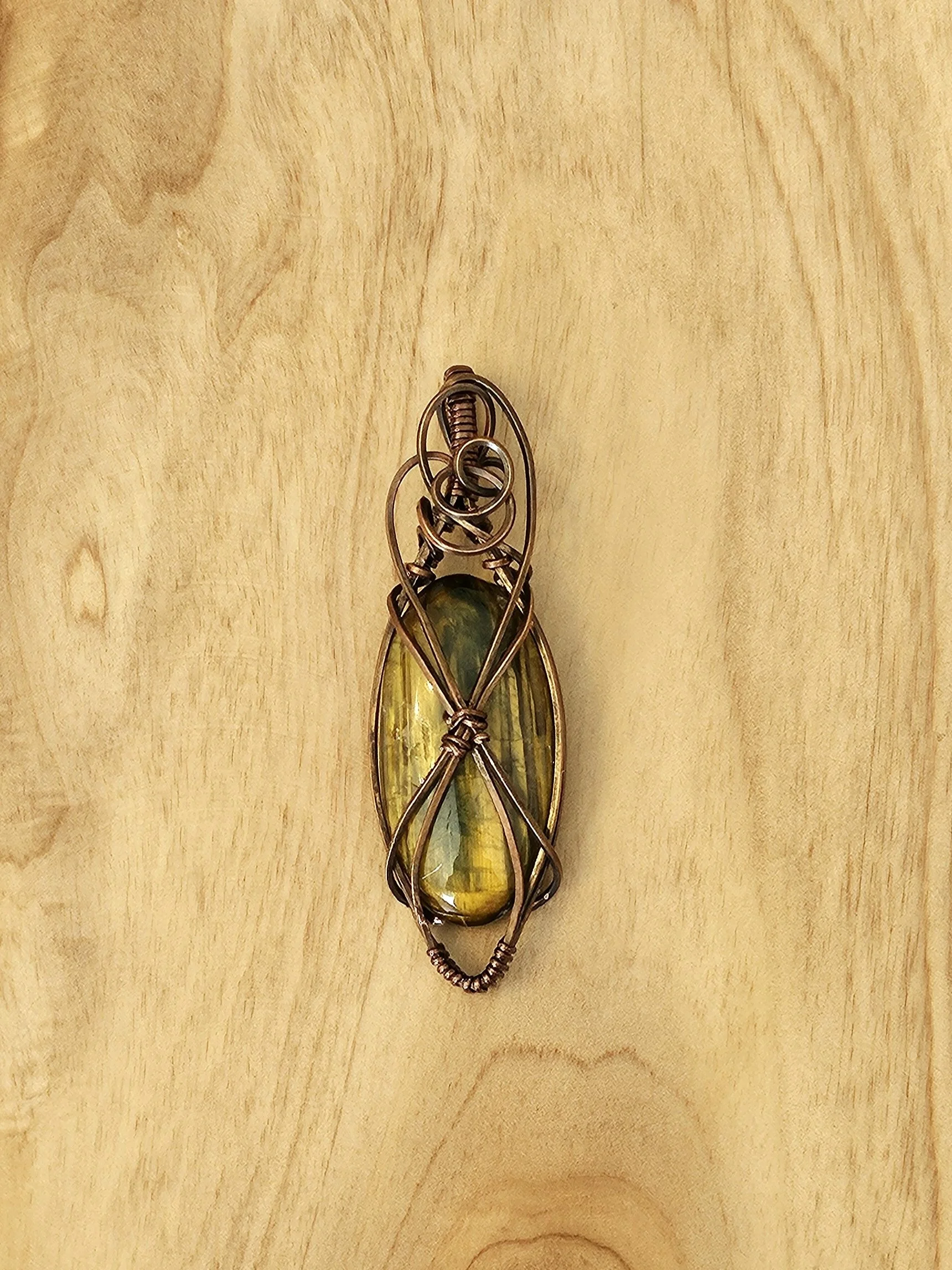 A wire-wrapped green and yellow stone brooch on a wooden surface.