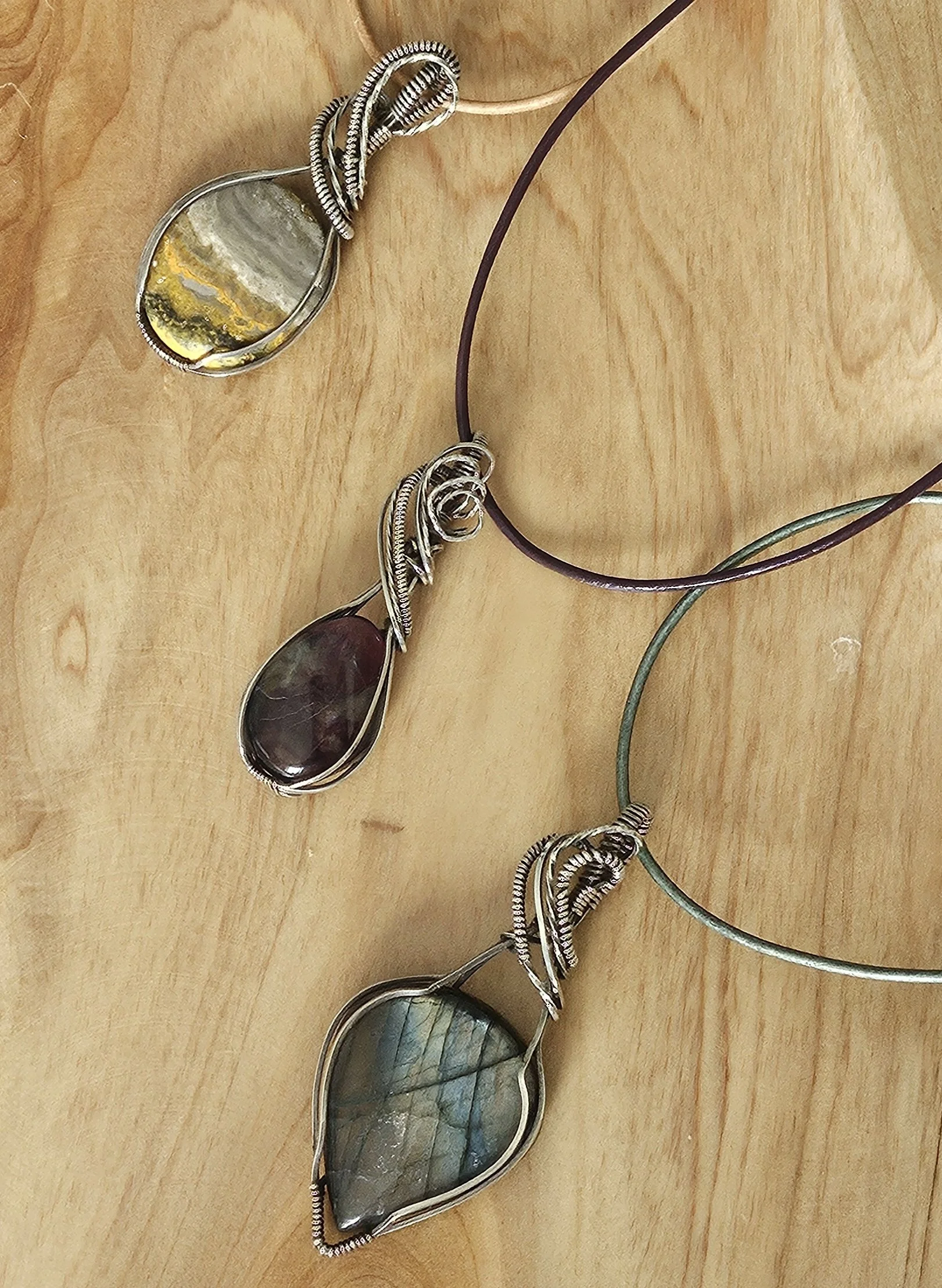 Two wire-wrapped gemstone necklaces with large polished stones on a wooden surface.
