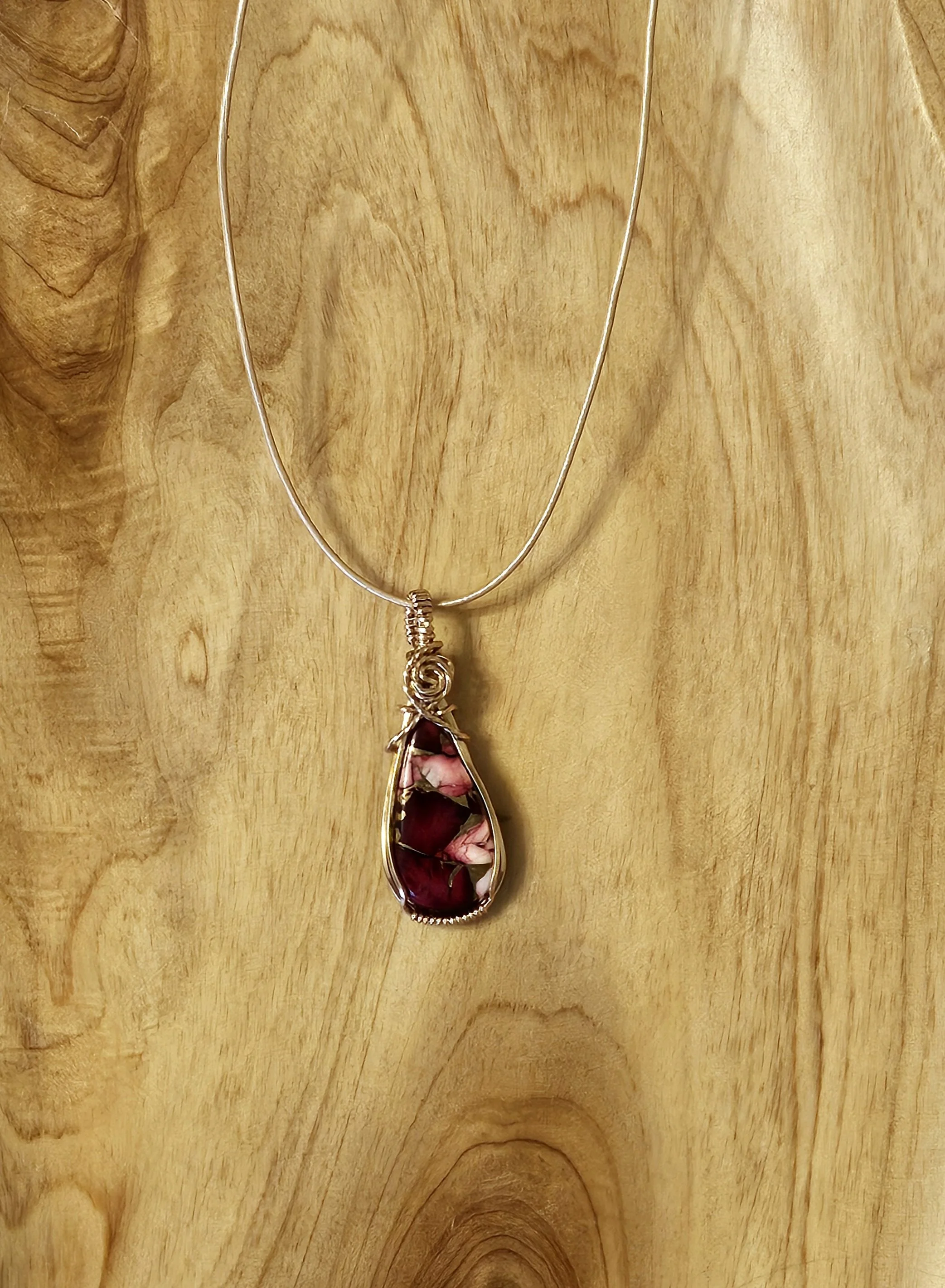 Silver necklace with a teardrop-shaped pendant containing pink and purple stones, hanging on a wooden surface.