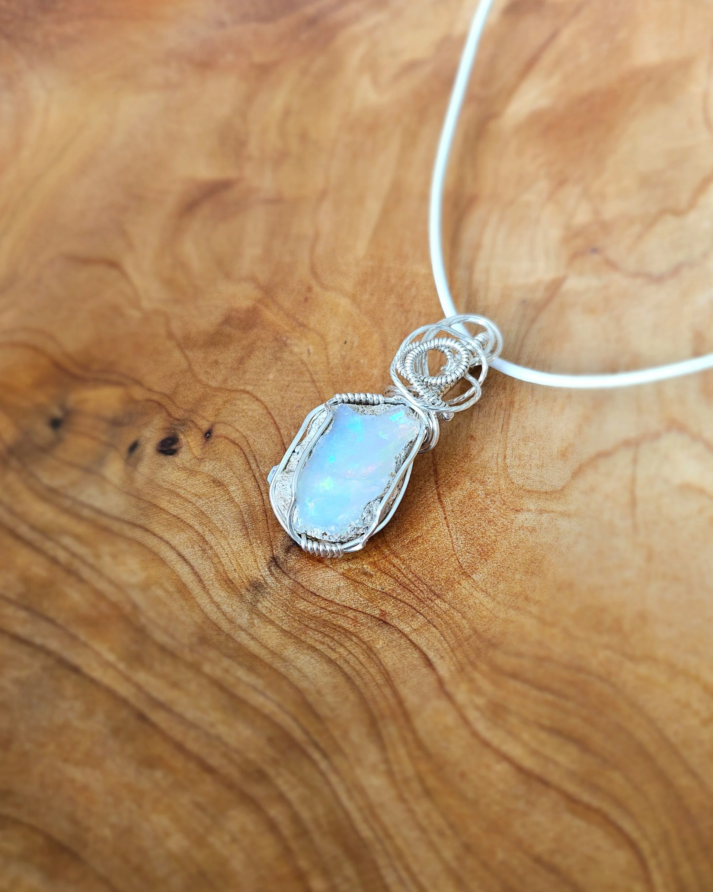 Silver wire-wrapped necklace with a large opal pendant on a wooden surface.