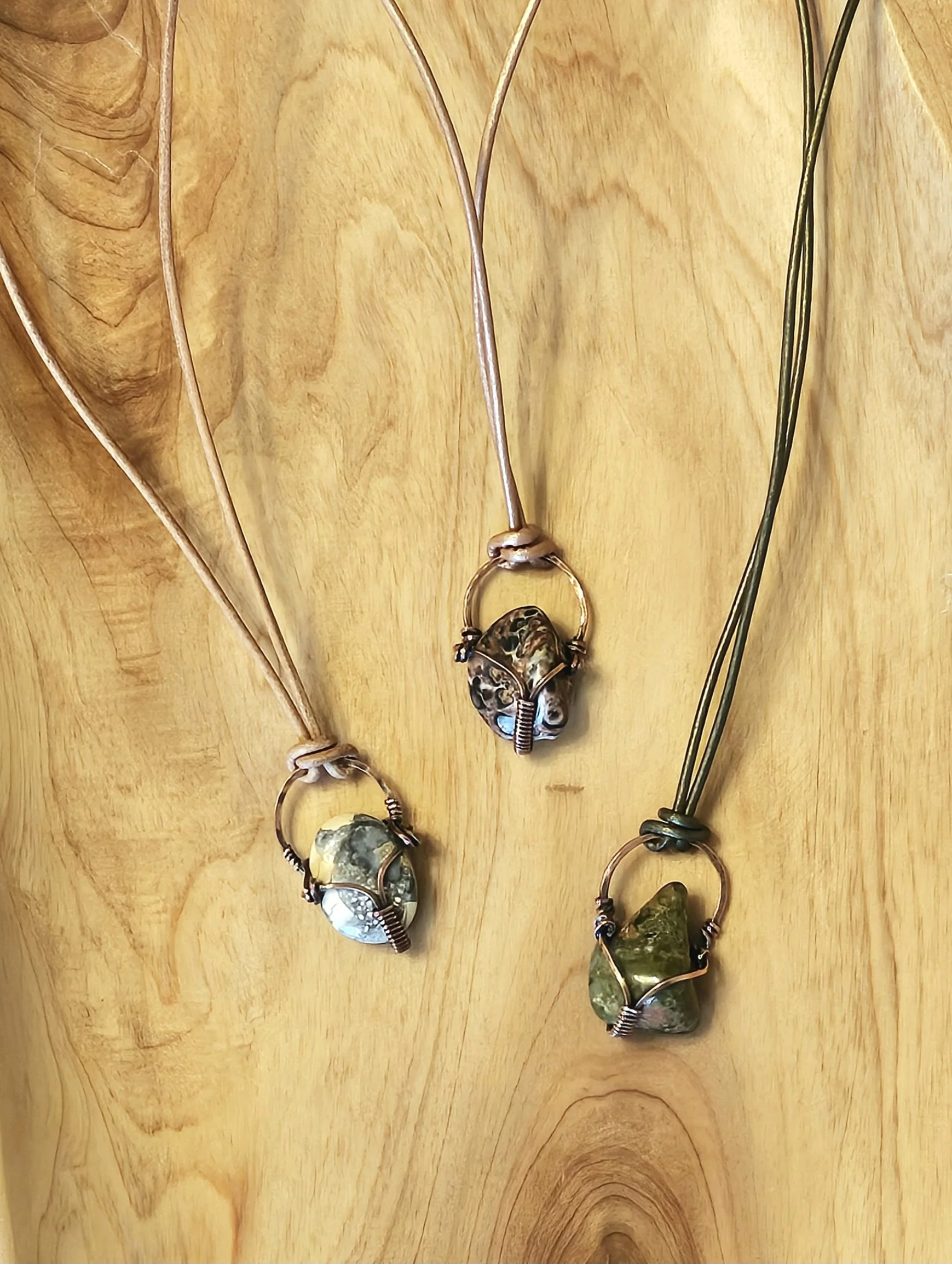 Three necklaces with wire-wrapped stones on a wooden surface.