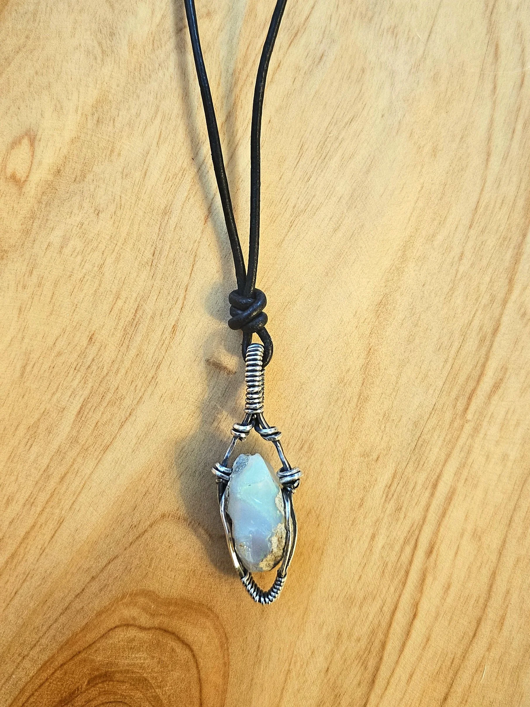 A pendant necklace with a large, irregularly shaped light blue stone wrapped in wire, hanging from a black cord.