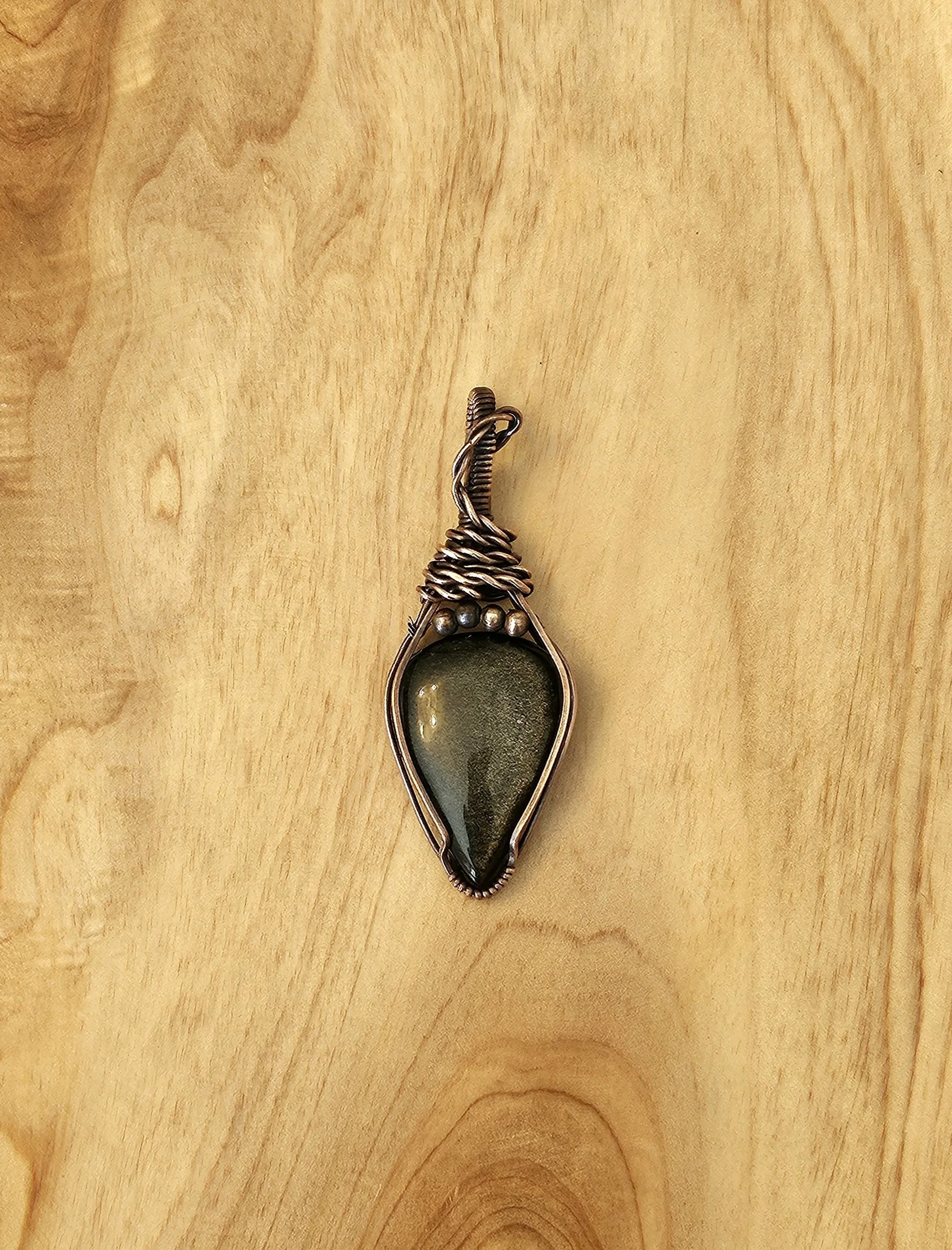 Wire-wrapped pendant with a dark green oval stone on a wooden surface.