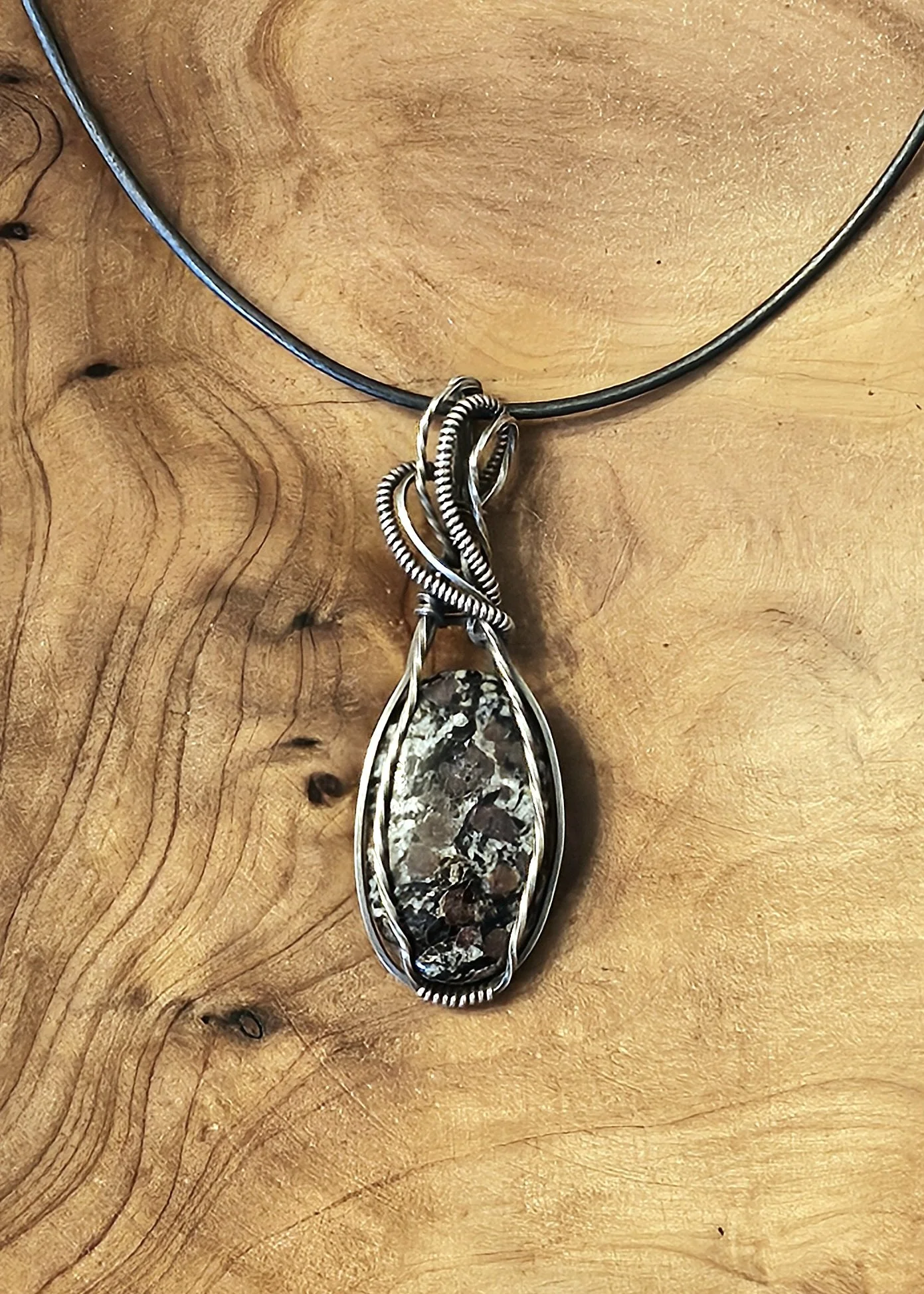 A silver necklace with a large stone pendant on a wooden surface.