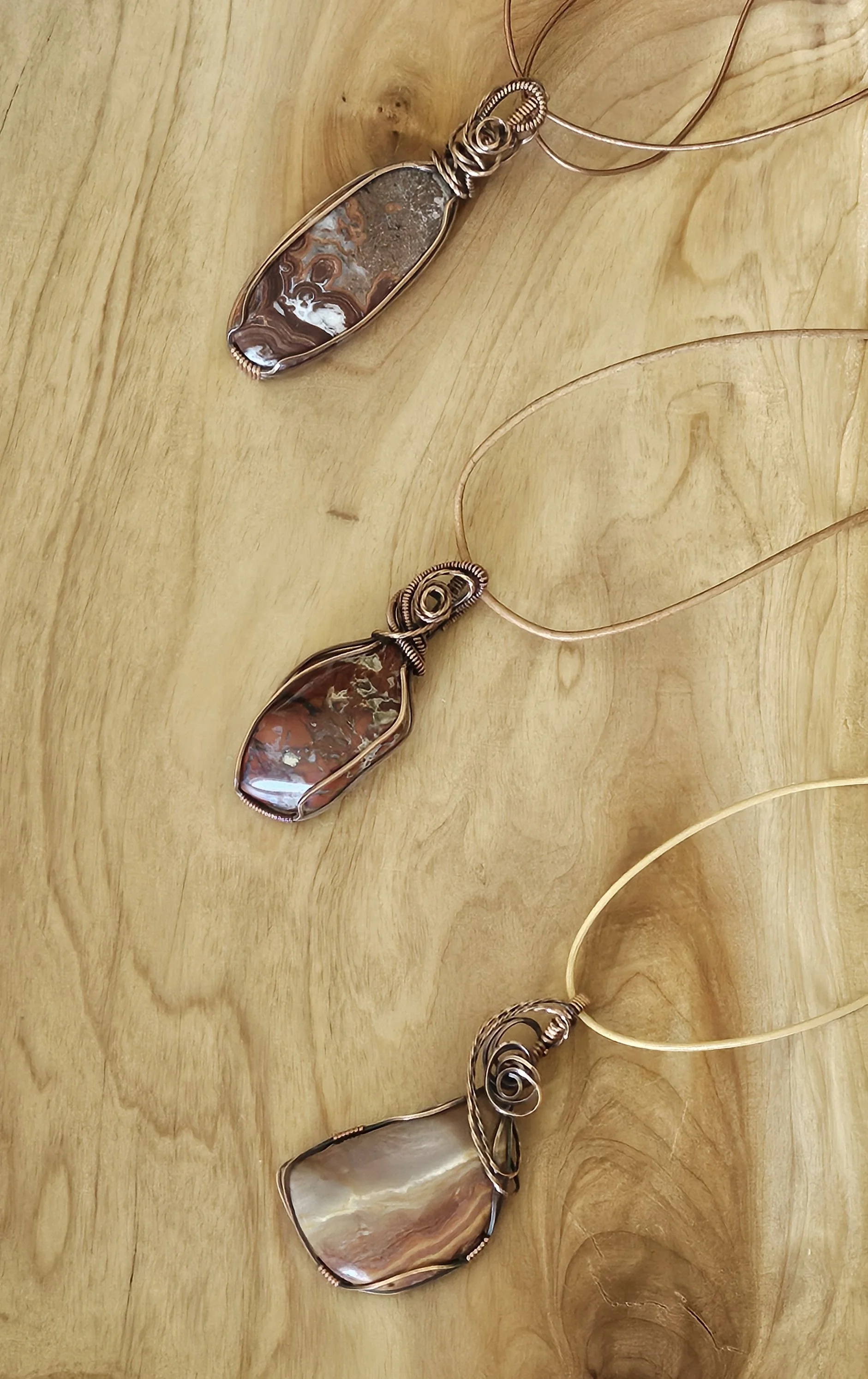 Three wire-wrapped necklaces with large stone pendants on a wooden surface.