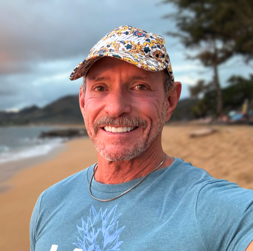 Close-up of a man outdoors with palm trees and a pool in the background.