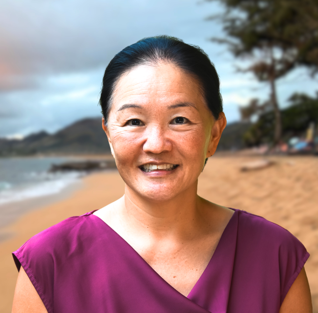 Close-up of a woman smiling at the beach during daytime with palm trees and a blue sky in the background.