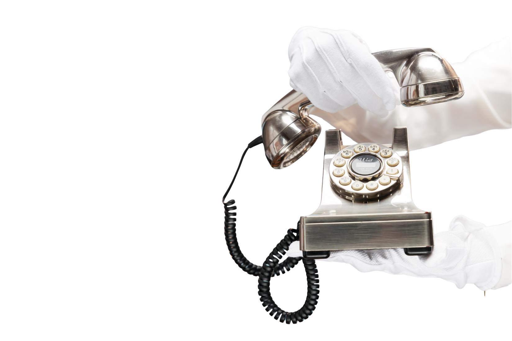 A vintage rotary telephone with a metal finish, being held by a person wearing white gloves.