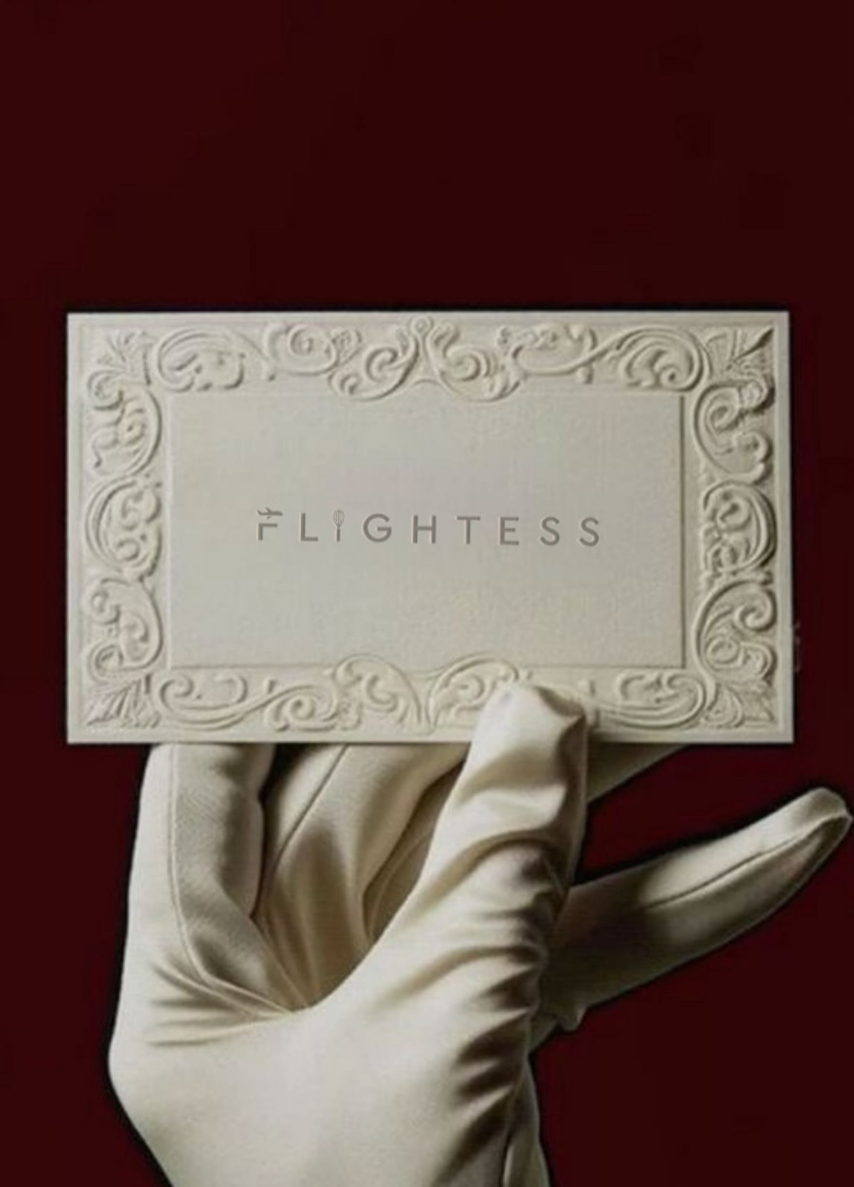 A hand wearing a white glove holding a rectangular box with ornate embossed border and the word 'FLIGHTESS' printed in the center, against a dark red background.