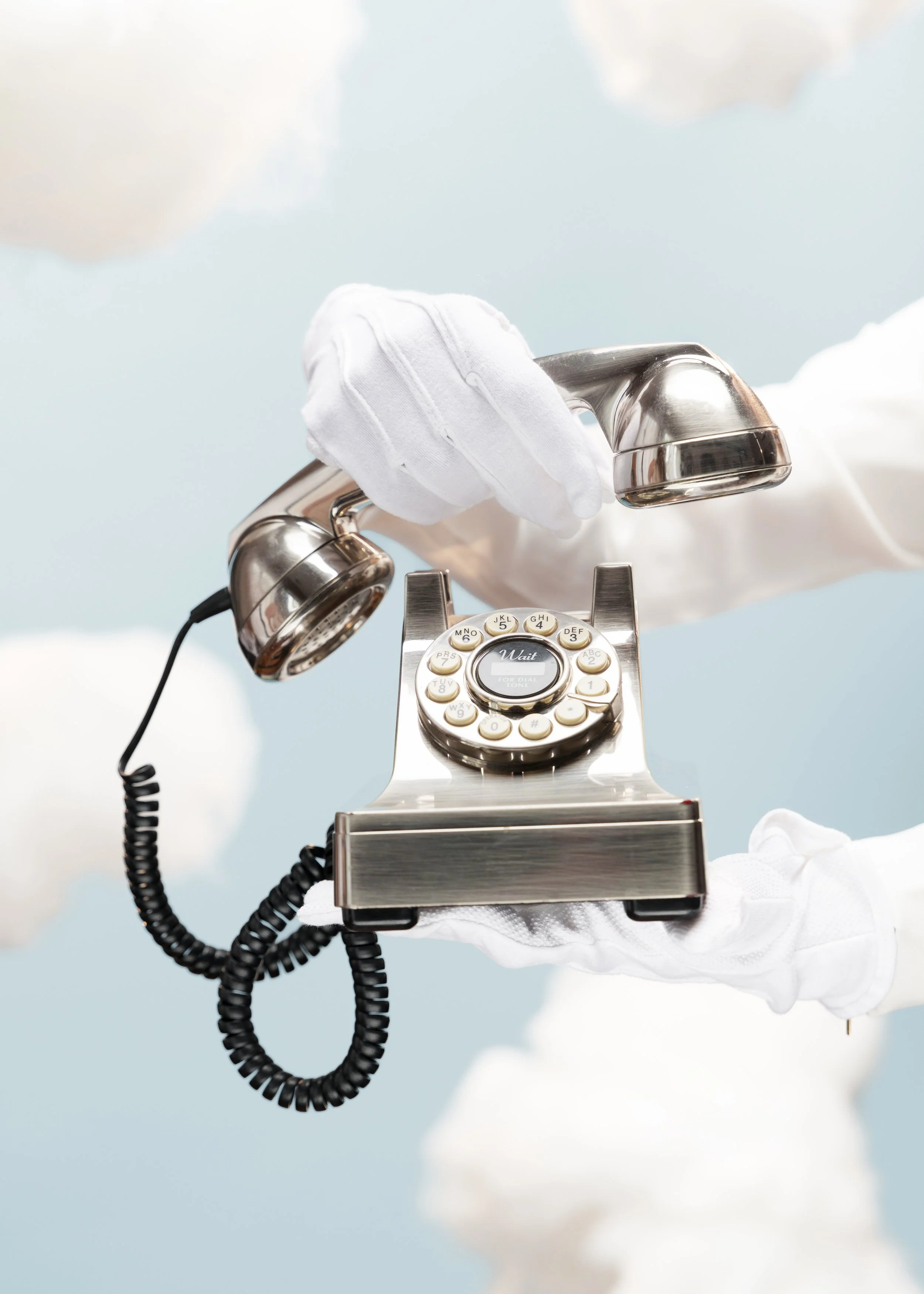 Person wearing white gloves holding a vintage rotary telephone with a starlight background and clouds.
